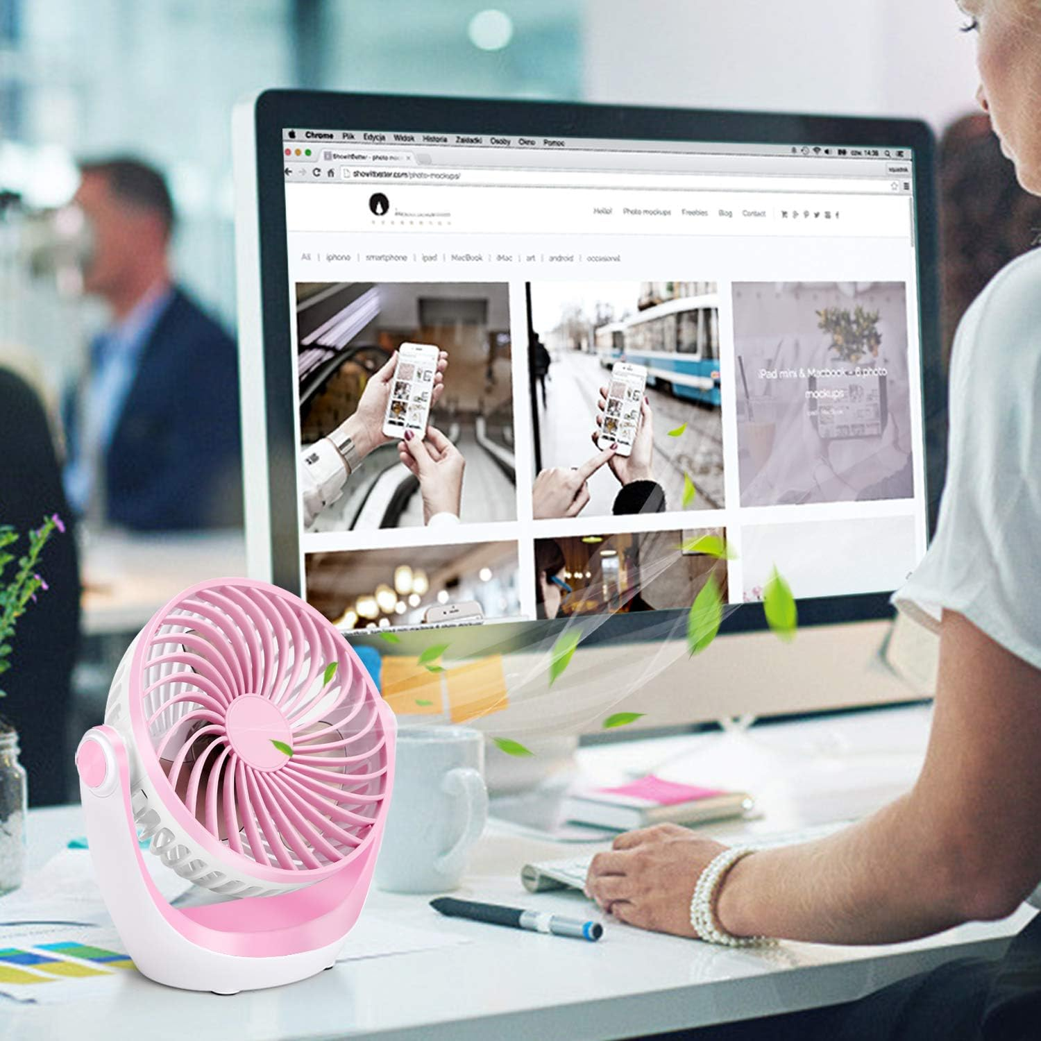 Ein kleiner pinker Ventilator steht auf einem Schreibtisch vor einem Computermonitor.
