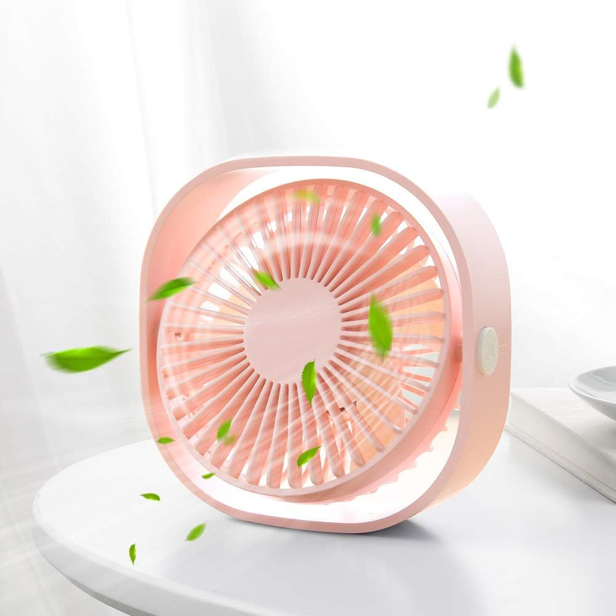 Ein kleiner rosafarbener Ventilator mit grünen Blättern, der auf einem weißen Tisch steht.
