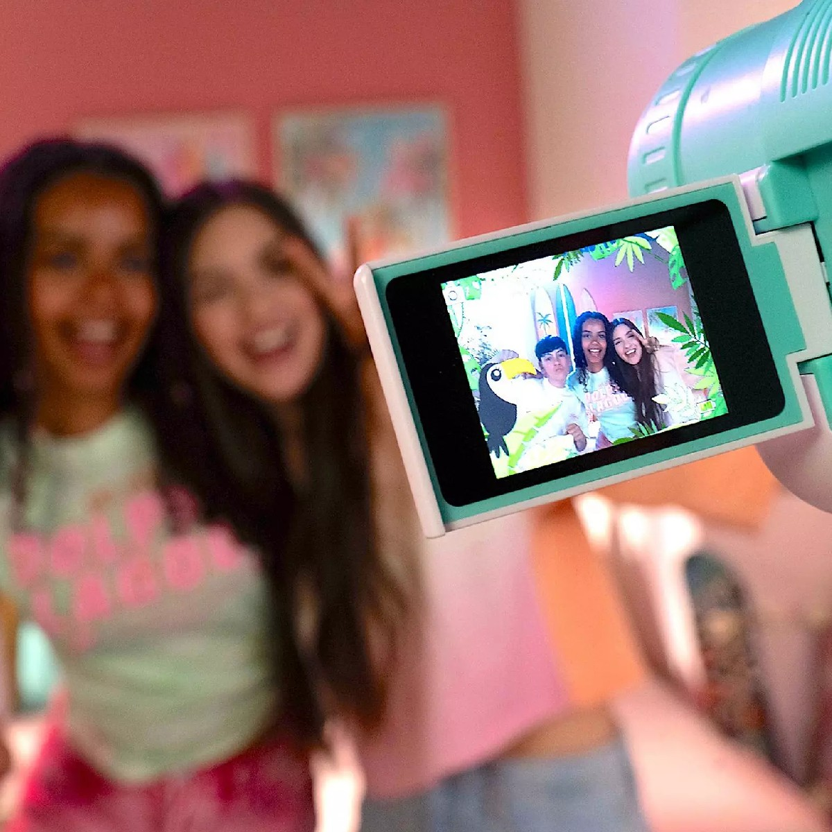 Tres niños sonriendo en la pantalla de una cámara verde menta, junto a dos chicas borrosas.