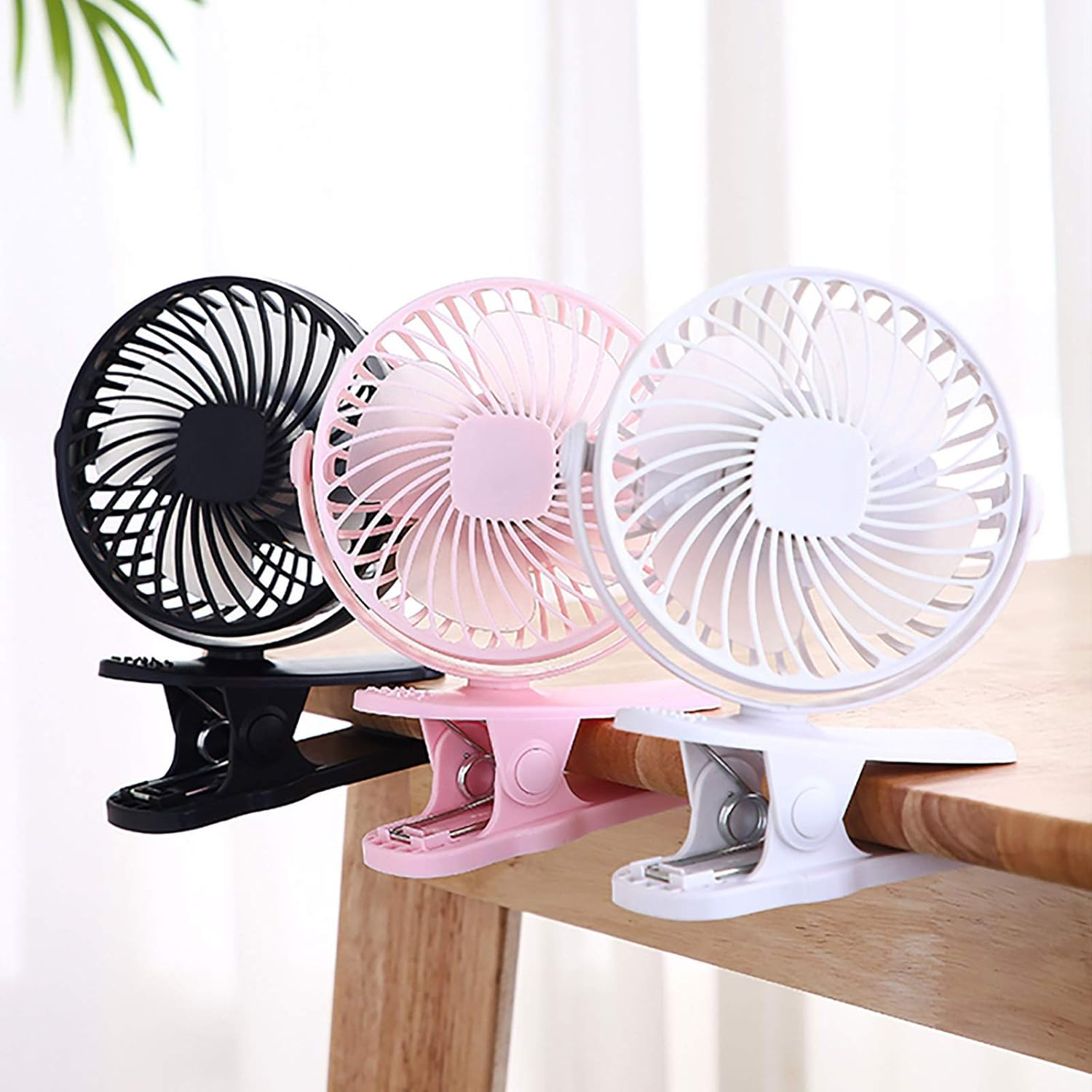 Drei Clip-Ventilatoren in Schwarz, Rosa und Weiß auf einem Holztisch.