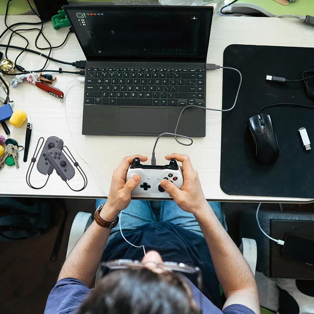 Person spielt Videospiele mit einem Controller, der an einen Laptop angeschlossen ist, mit Maus und USB-Sticks in der Nähe.