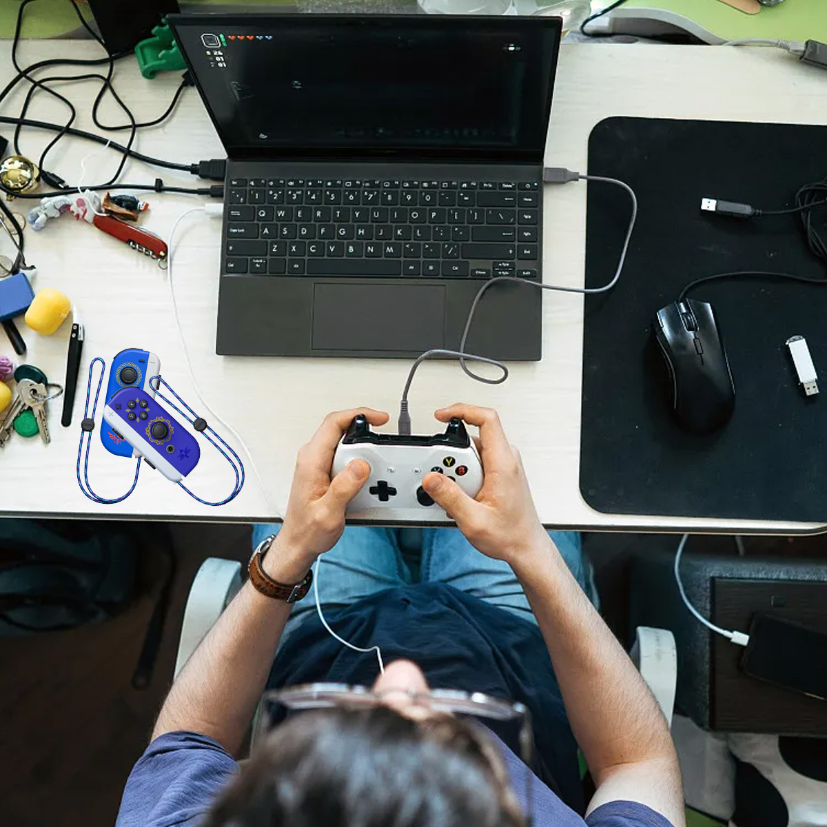 Person spielt Videospiel mit weißem Controller, verbunden mit Laptop. Blauer Controller in der Nähe.
