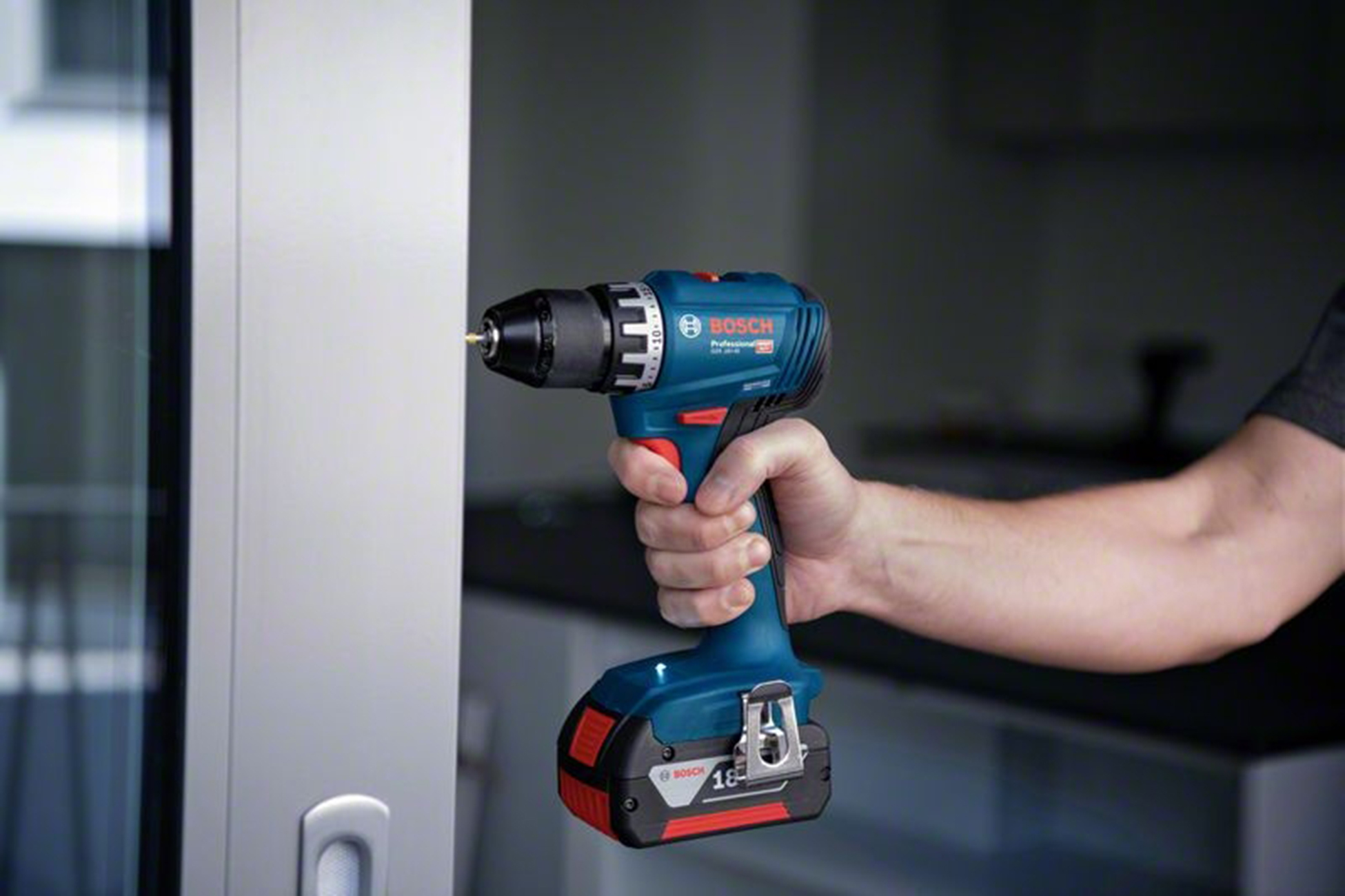 Una mano tiene un trapano avvitatore a batteria Bosch blu contro un muro bianco.