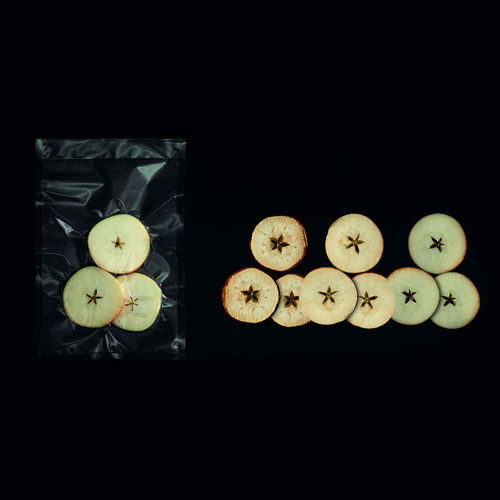 Rodajas de manzana secas en una bolsa y alineadas sobre fondo negro.