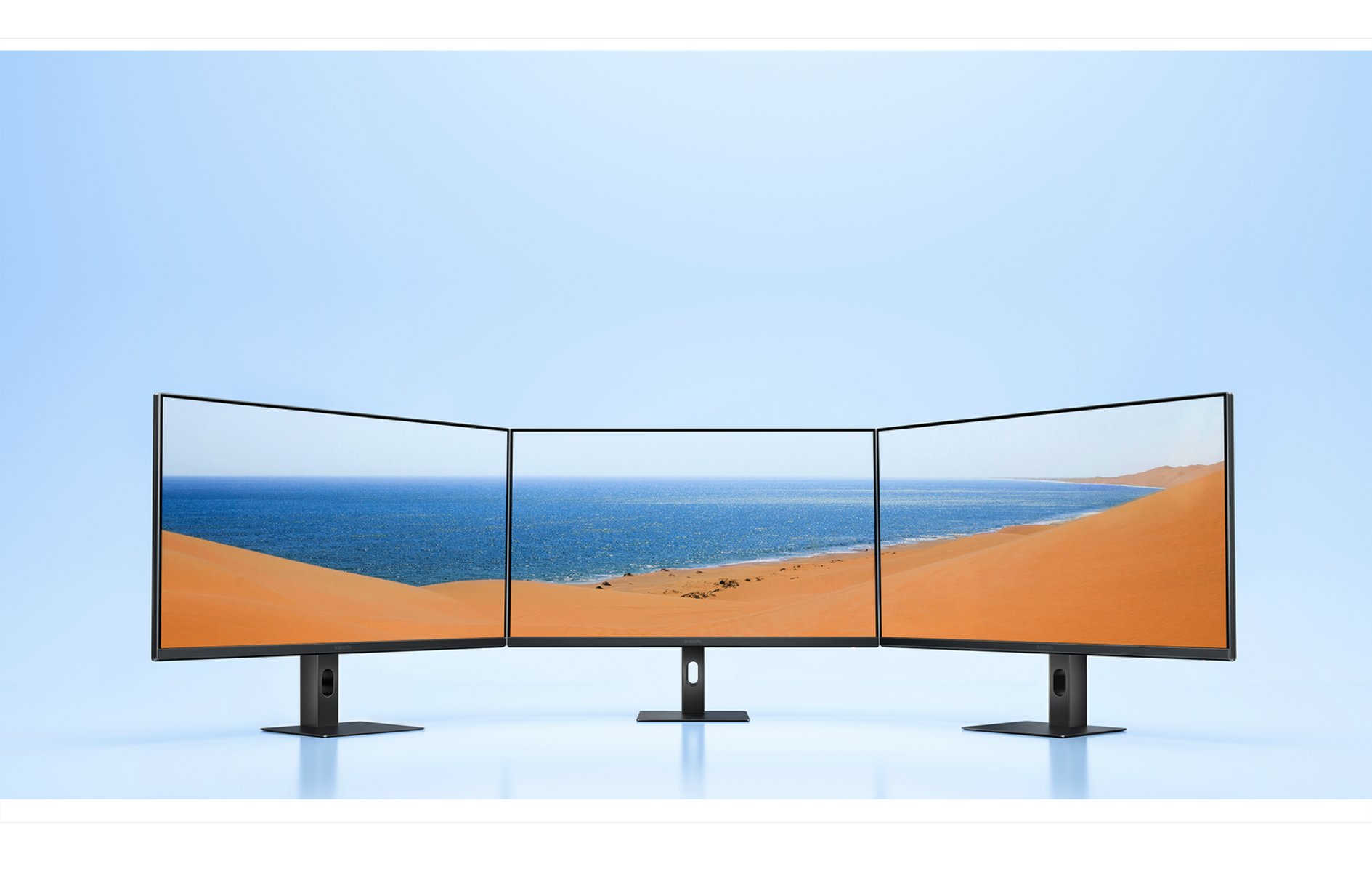 Trzy monitory wyświetlają spokojną scenę plażową z niebieską wodą i wydmami.