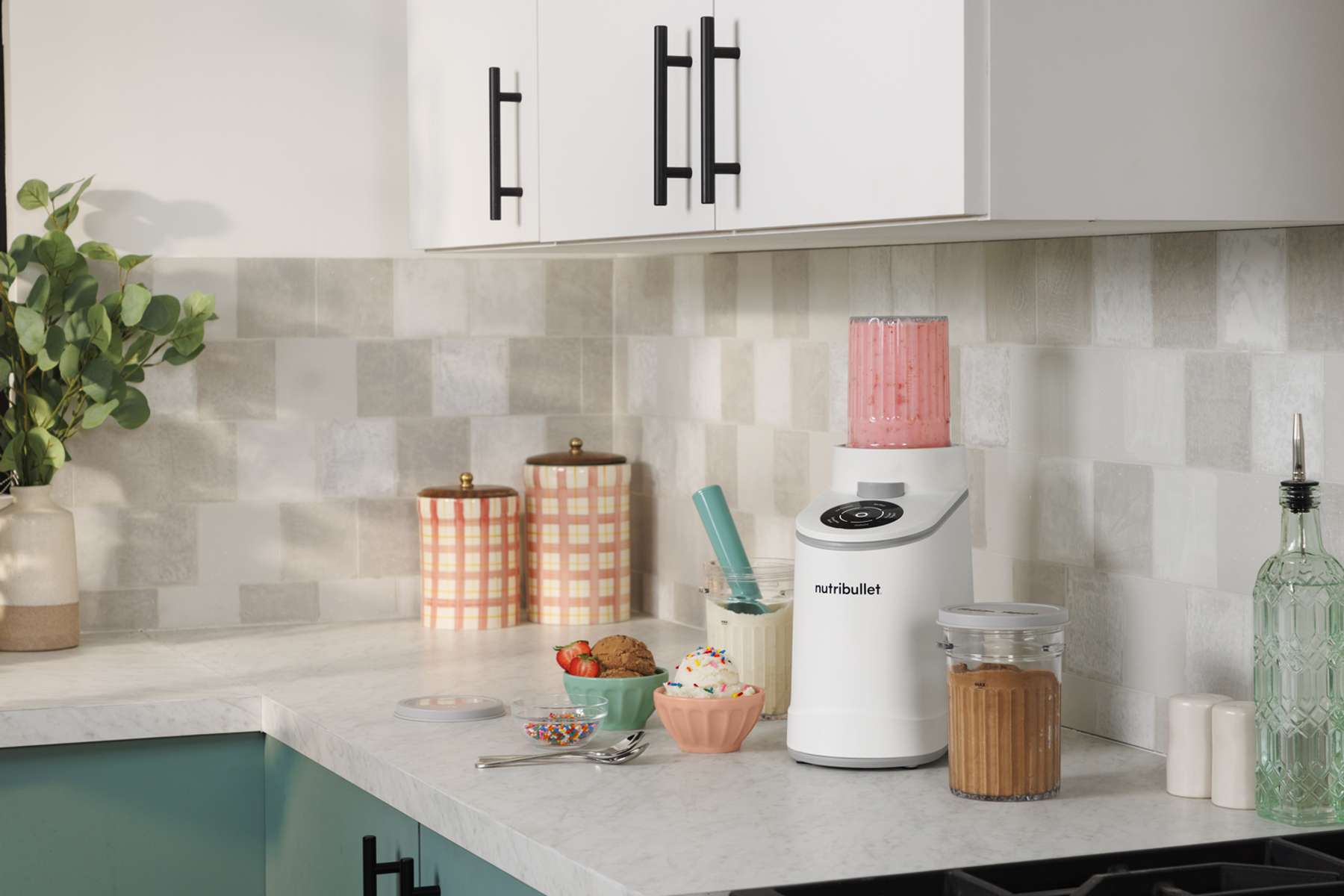 Ein weißer Nutribullet-Mixer mit rosa Smoothie, daneben Eiscreme, Kekse und Streusel.