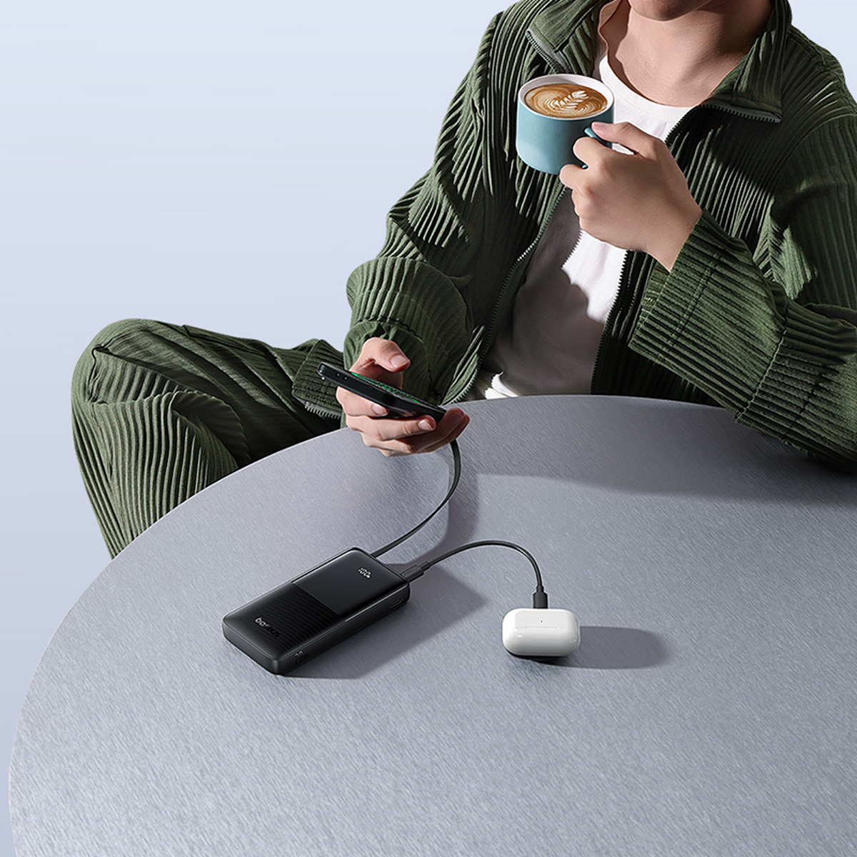 Uomo beve caffè, tiene telefono collegato a power bank e custodia auricolari.