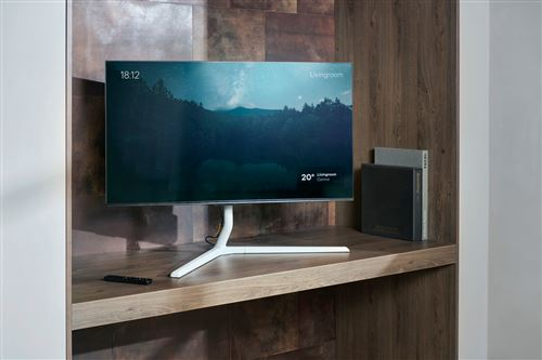Ein moderner Fernseher mit weißem Standfuß steht auf einem Holzregal. Eine Fernbedienung liegt davor.