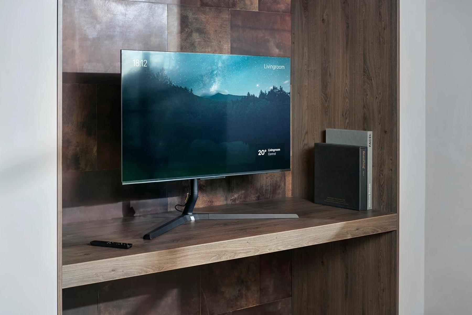 Ein moderner Monitor steht auf einem Holzregal, daneben Bücher und eine Fernbedienung.