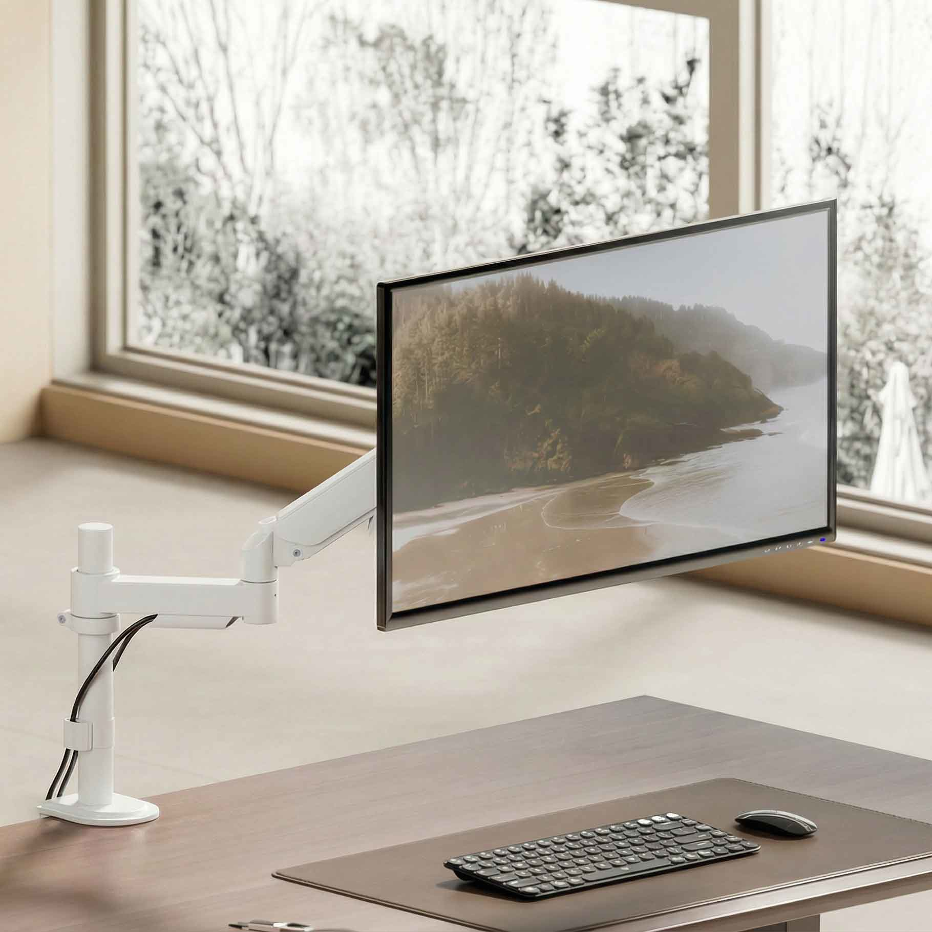 Un brazo de monitor blanco sostiene una pantalla con vista al paisaje, sobre un escritorio con teclado.