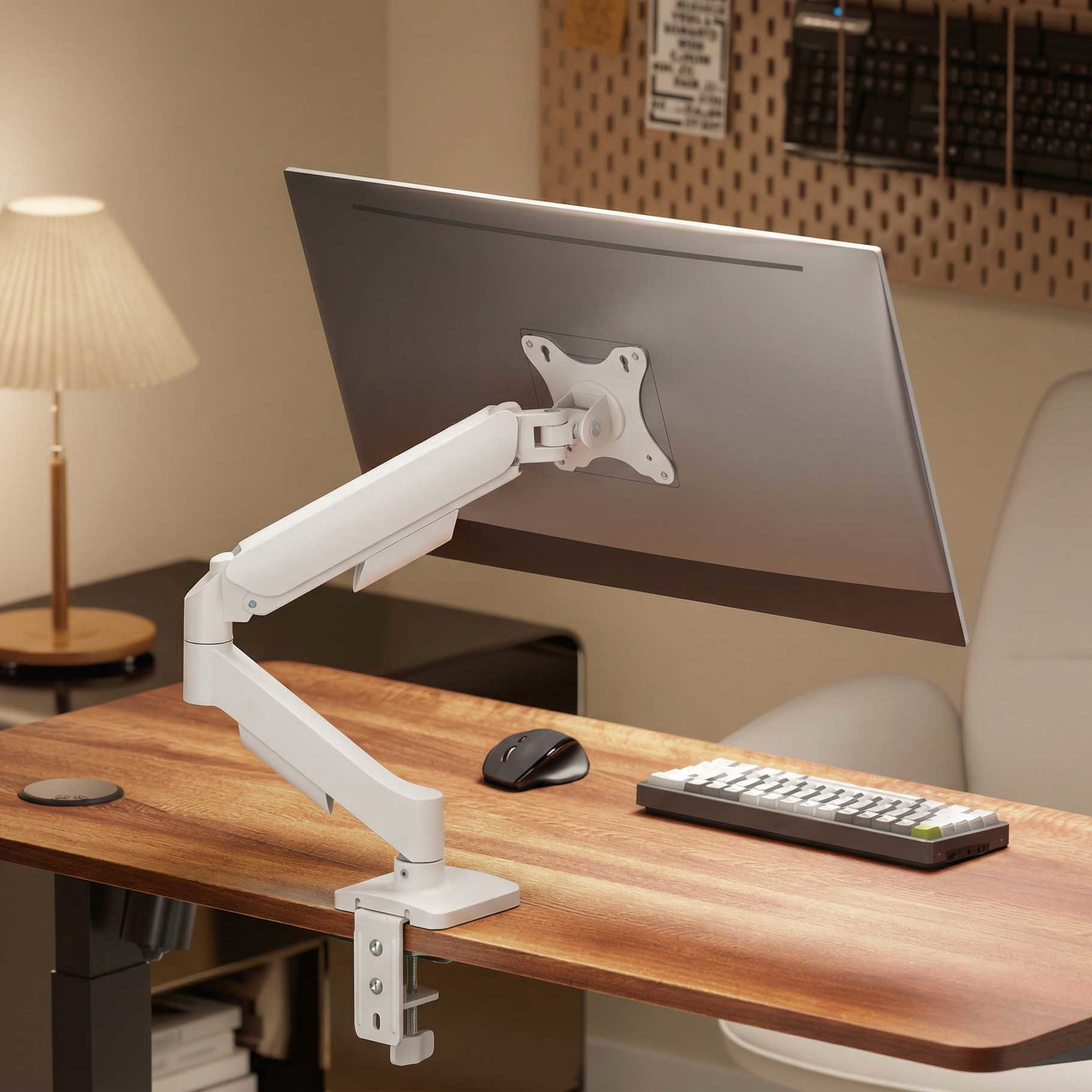 Un brazo de monitor blanco sostiene una pantalla plateada sobre un escritorio de madera.