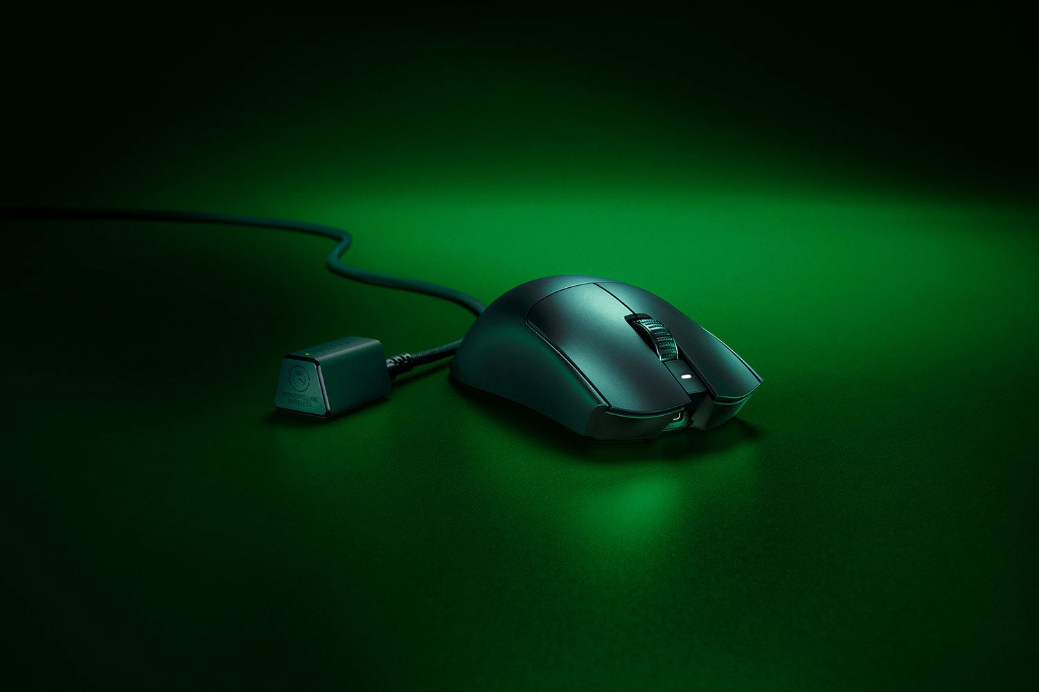 Un mouse gaming nero cablato con dongle su una superficie verde.