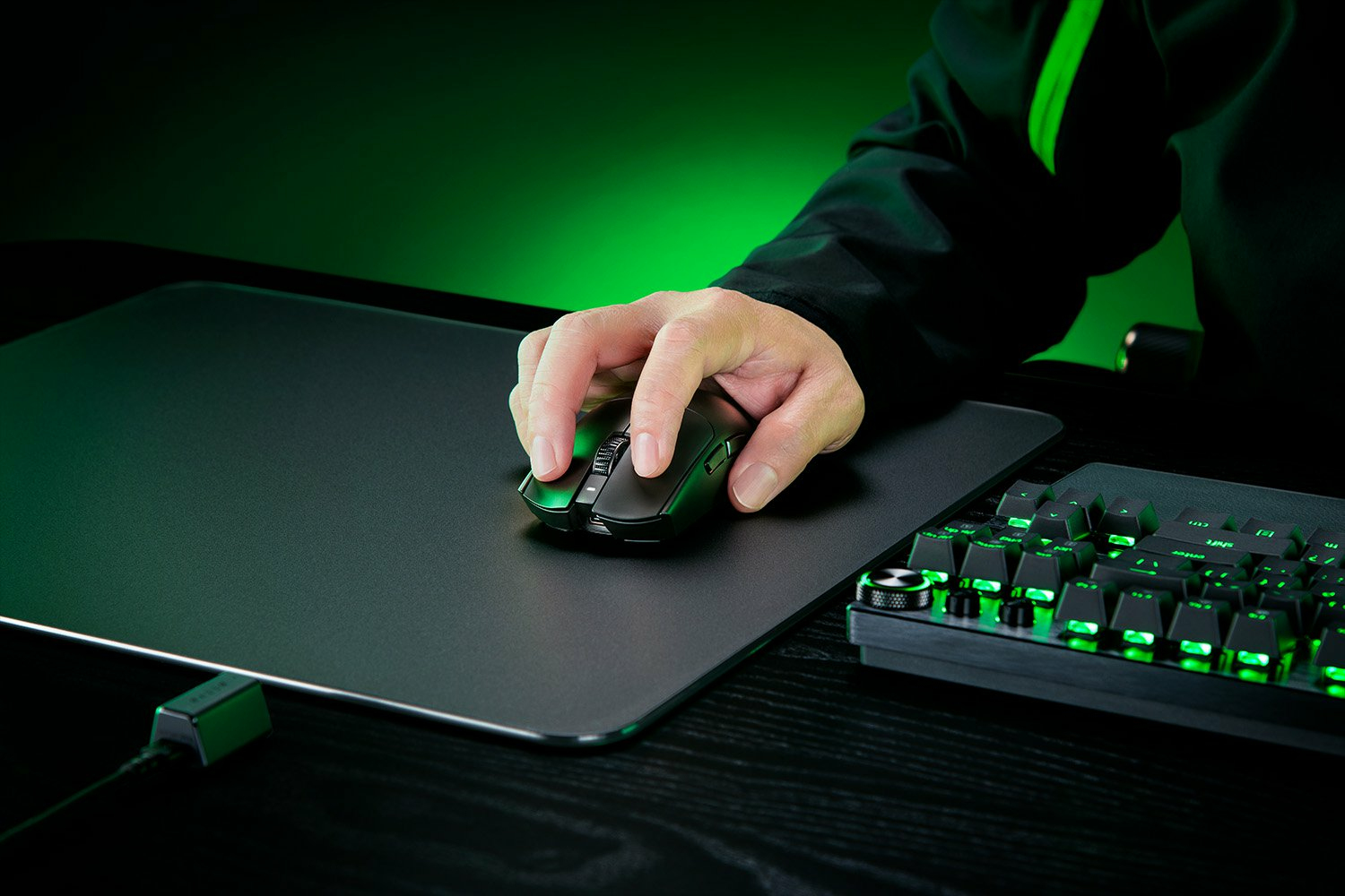 Una mano usa un mouse da gaming nero su un tappetino nero accanto a una tastiera illuminata di verde.