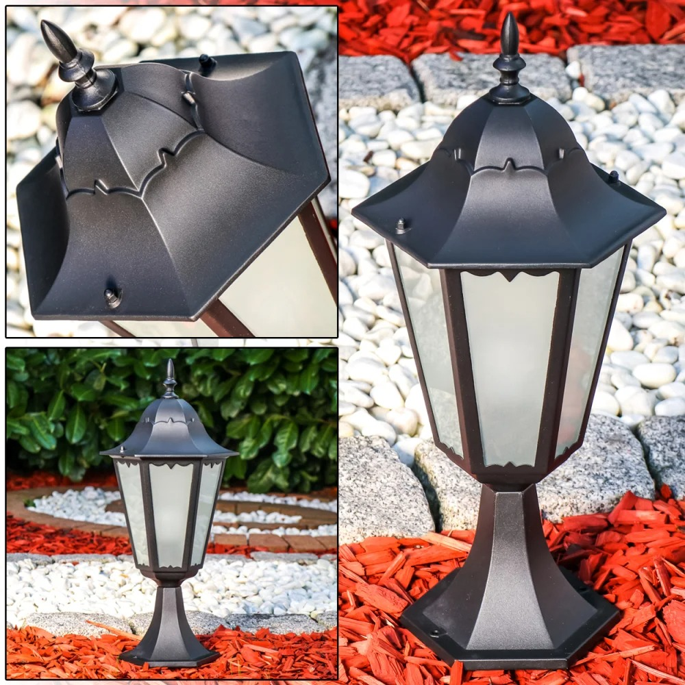 Schwarze Außenleuchte mit sechseckigem Glas und Zierspitze, auf Kies und Rindenmulch.