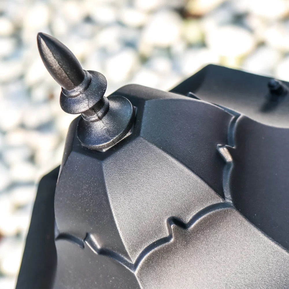 Ein schwarzer metallischer Zieraufsatz mit spitzem Ende auf einem geometrischen Objekt.