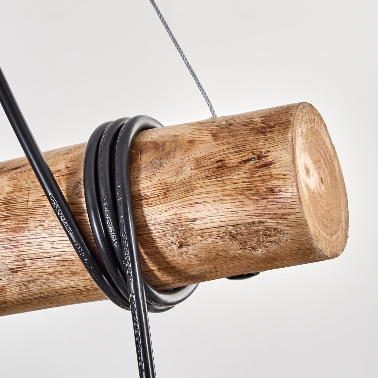 Ein dunkles Kabel ist um einen groben Holzstamm gewickelt, der an einem dünnen Draht hängt.