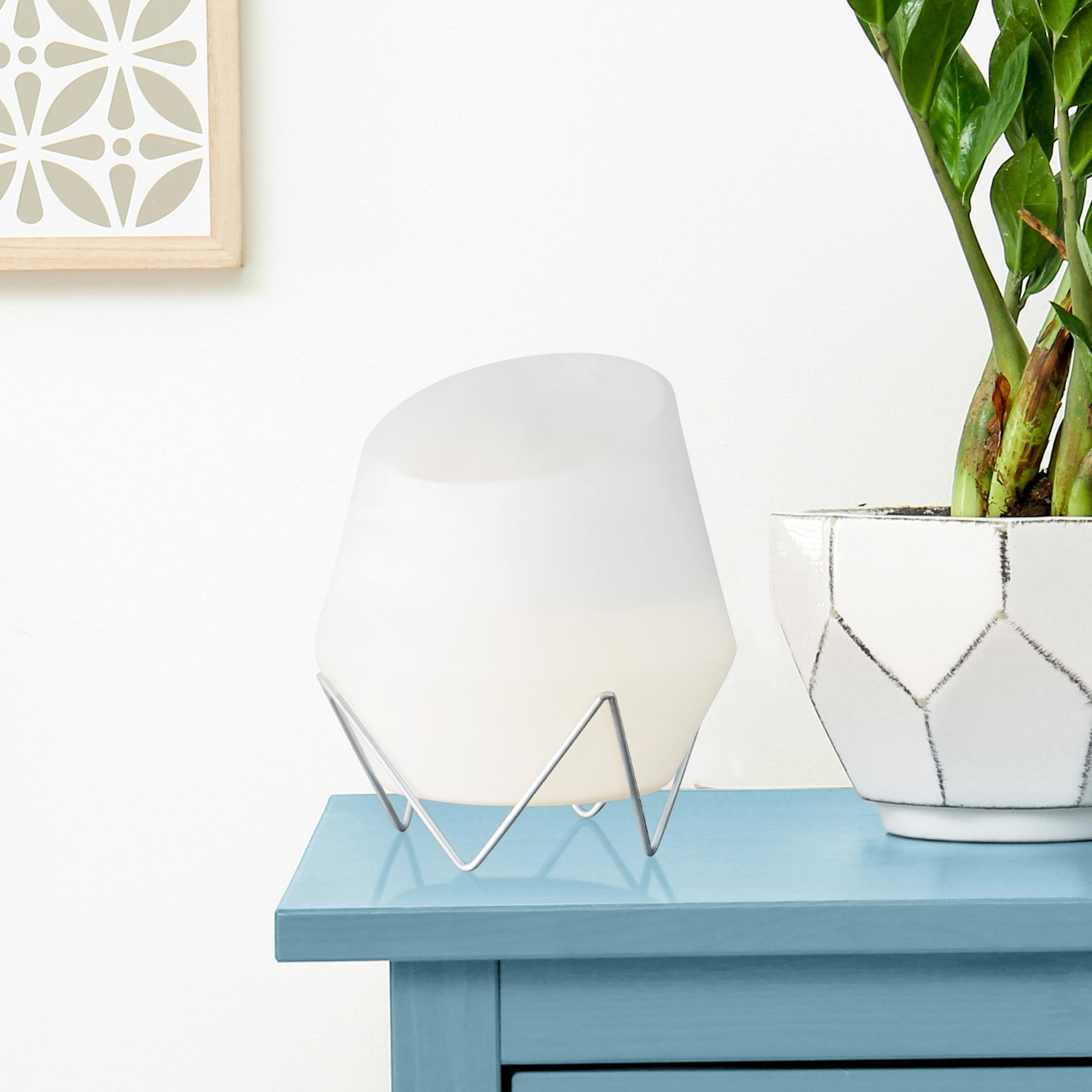 Lampe en verre dépoli blanc sur table bleue près d'une plante.