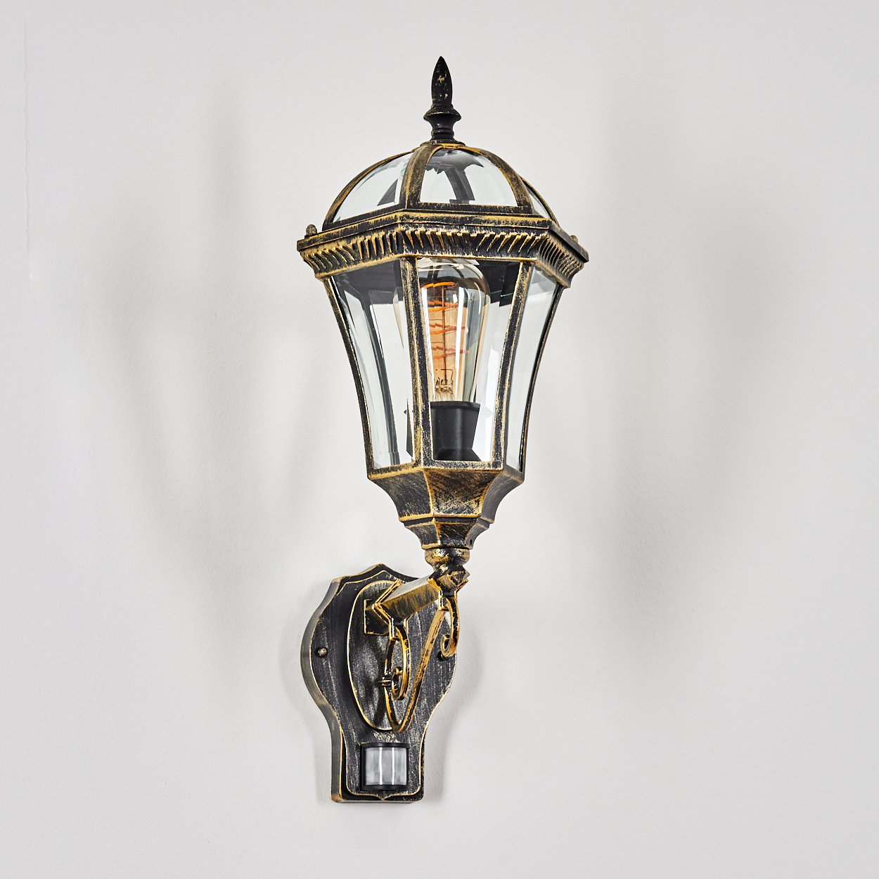Eine schwarze und goldene Wandlaterne im Vintage-Stil mit Glaskuppel und sichtbarer Glühbirne.