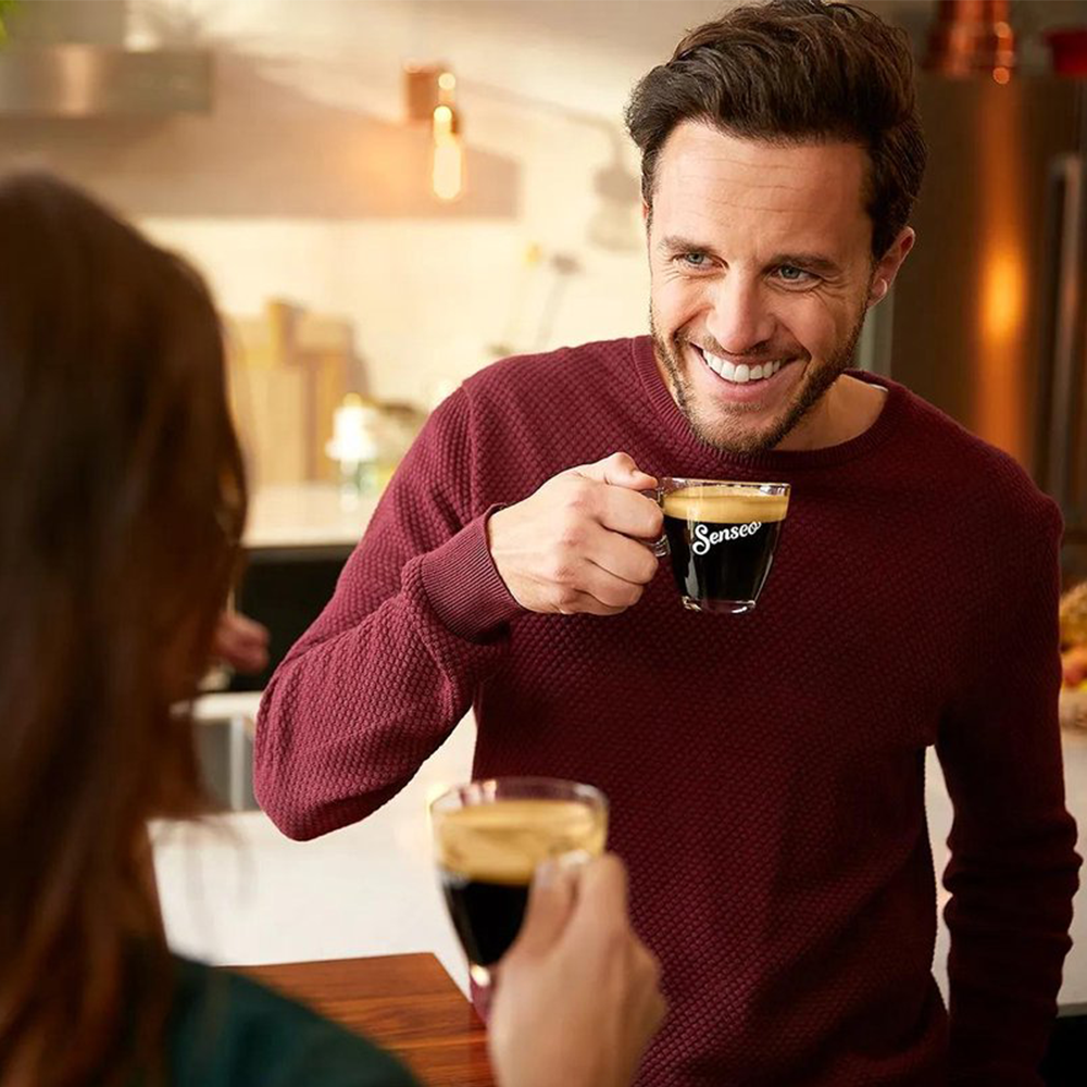 Ein Mann mit einem roten Pullover hält eine Kaffeetasse und lächelt.