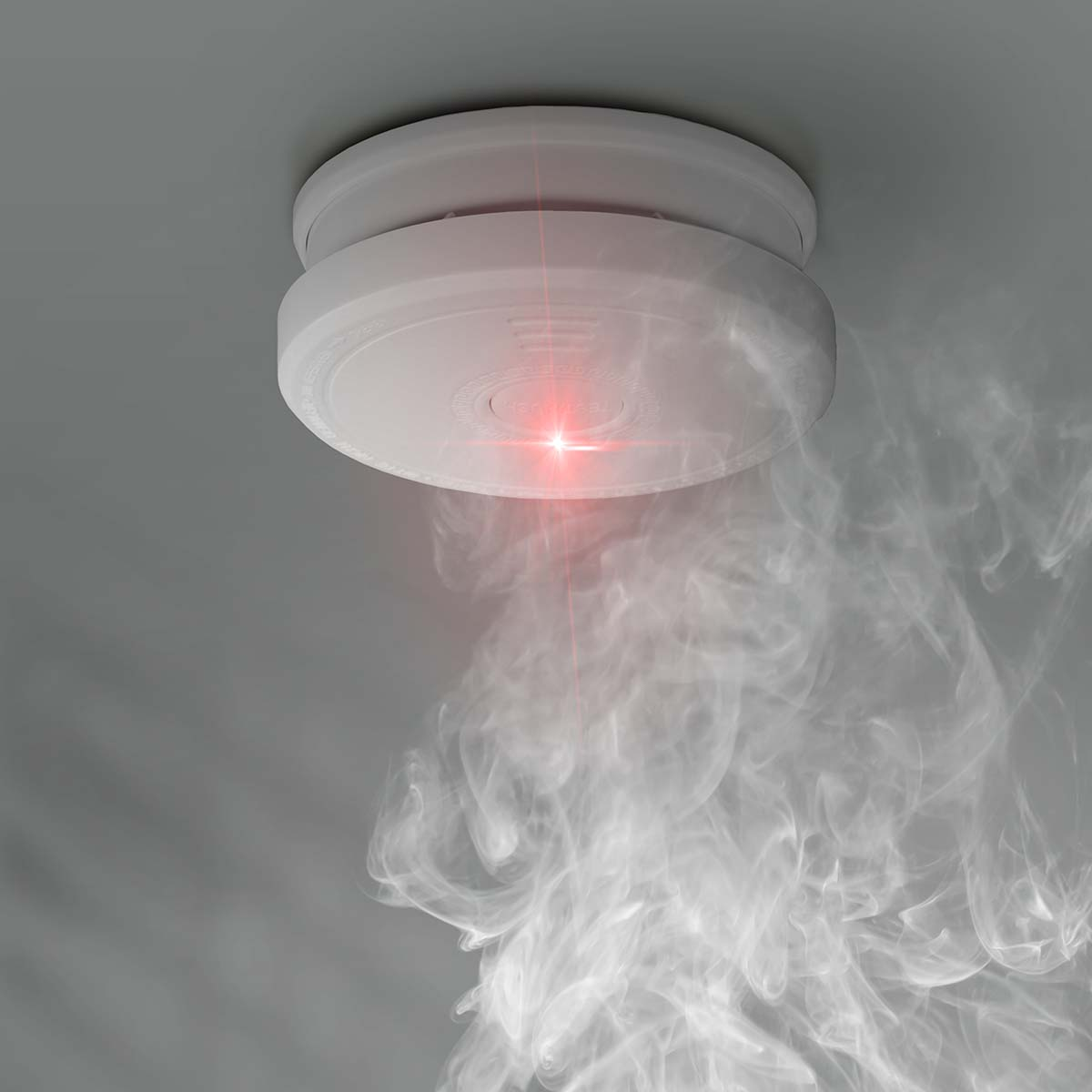 Rauchmelder mit rotem Licht und aufsteigendem Rauch an einer Decke.