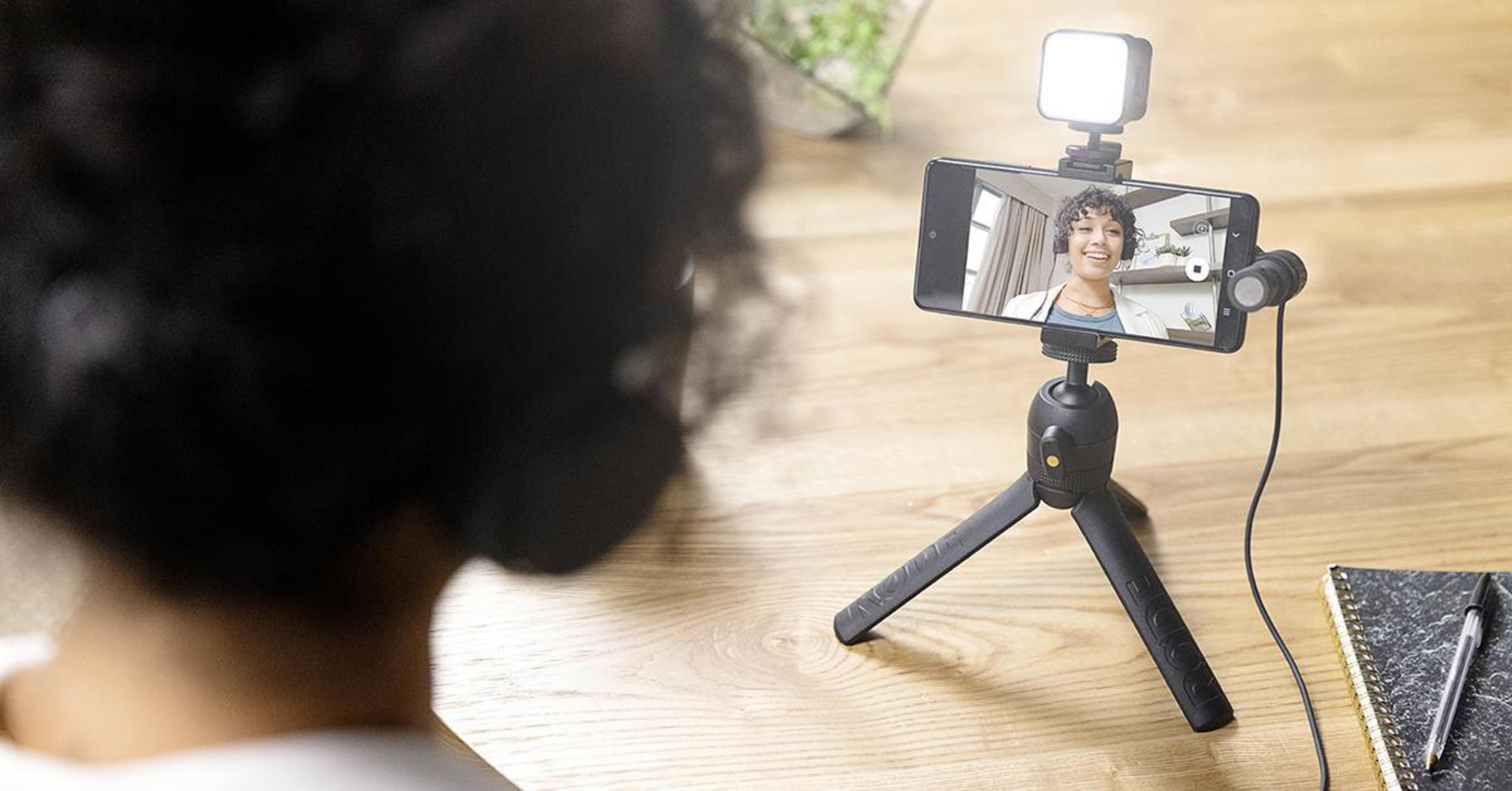 Una donna si filma su uno smartphone su un treppiede. Una luce è attaccata.