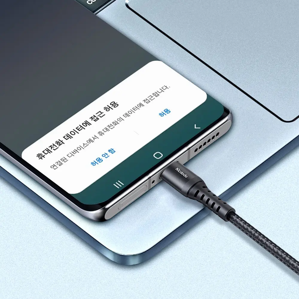 Ein Handy-Ladekabel wird in ein Smartphone gesteckt, das auf einem Laptop liegt.