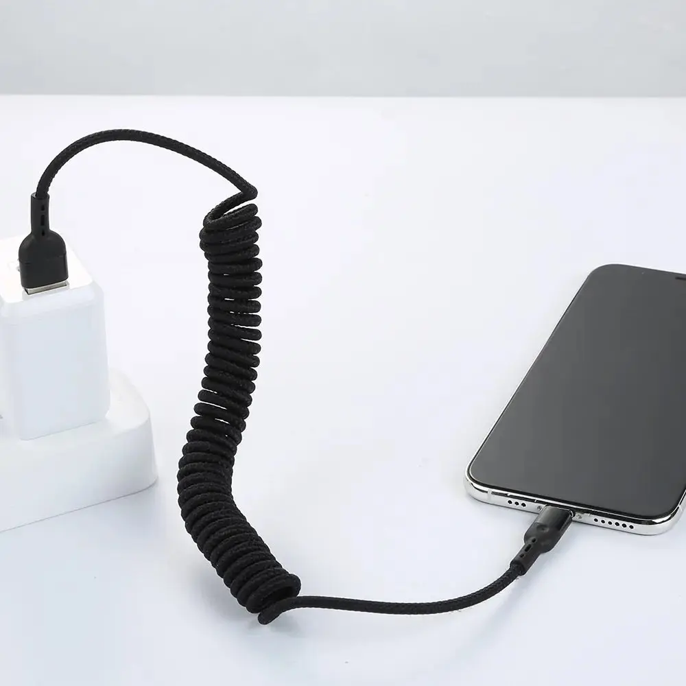 Siyah sarmal şarj kablosu, telefonu beyaz bir güç adaptörüne bağlıyor.