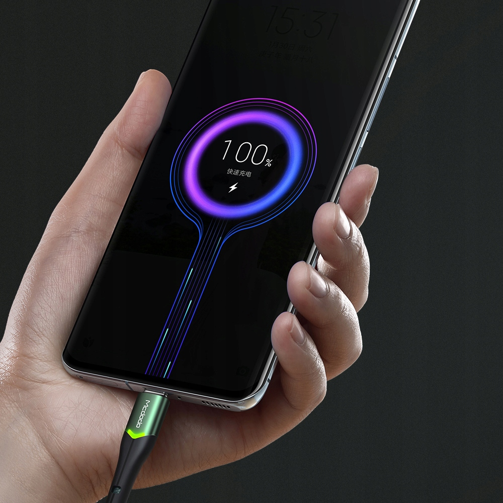 Bir el, yeşil ve siyah şarj kablosuna takılı bir telefon tutuyor. Telefon %100 şarj olduğunu gösteriyor.