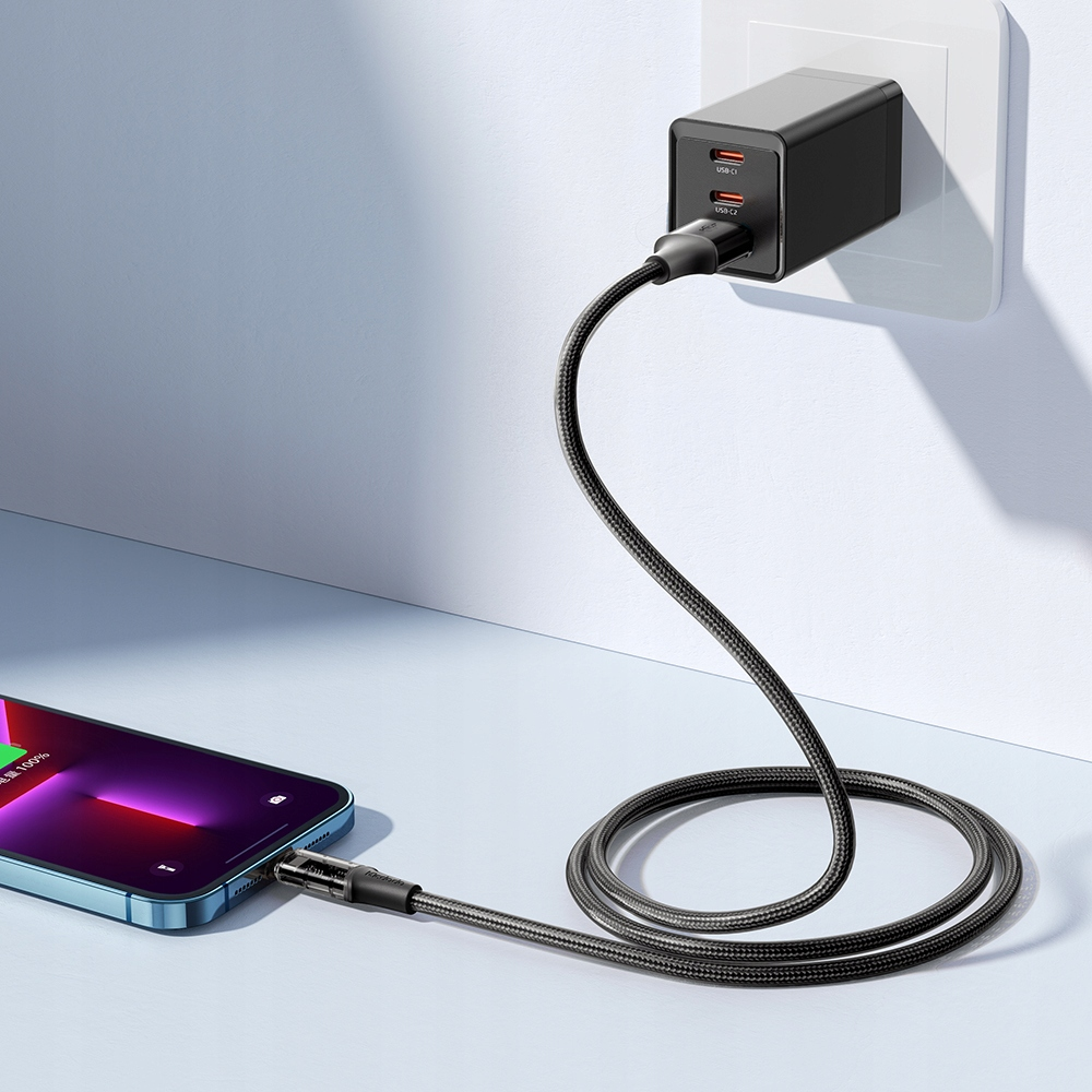 İki USB-C portlu siyah şarj cihazı, beyaz bir duvara prizine takılı, telefon şarj ediyor.