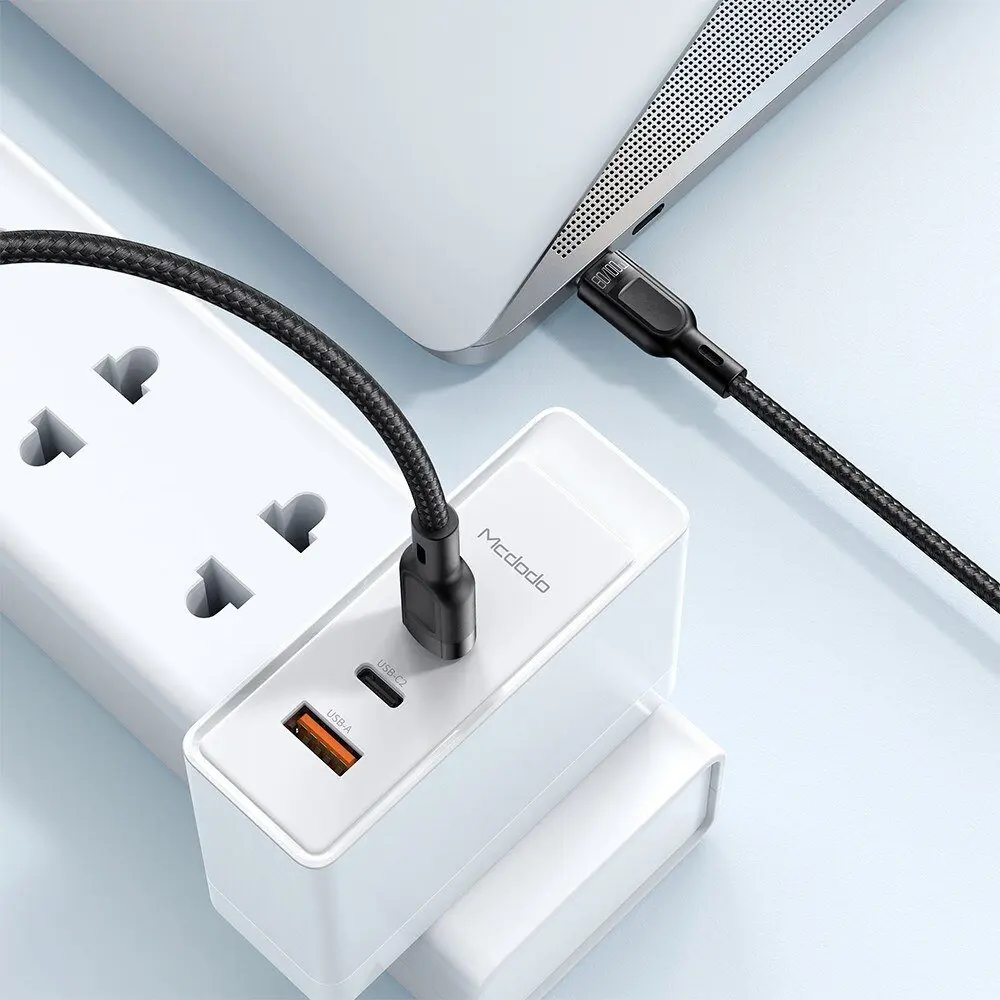 Siyah bir USB-C kablosu beyaz bir şarj cihazını dizüstü bilgisayara bağlıyor.