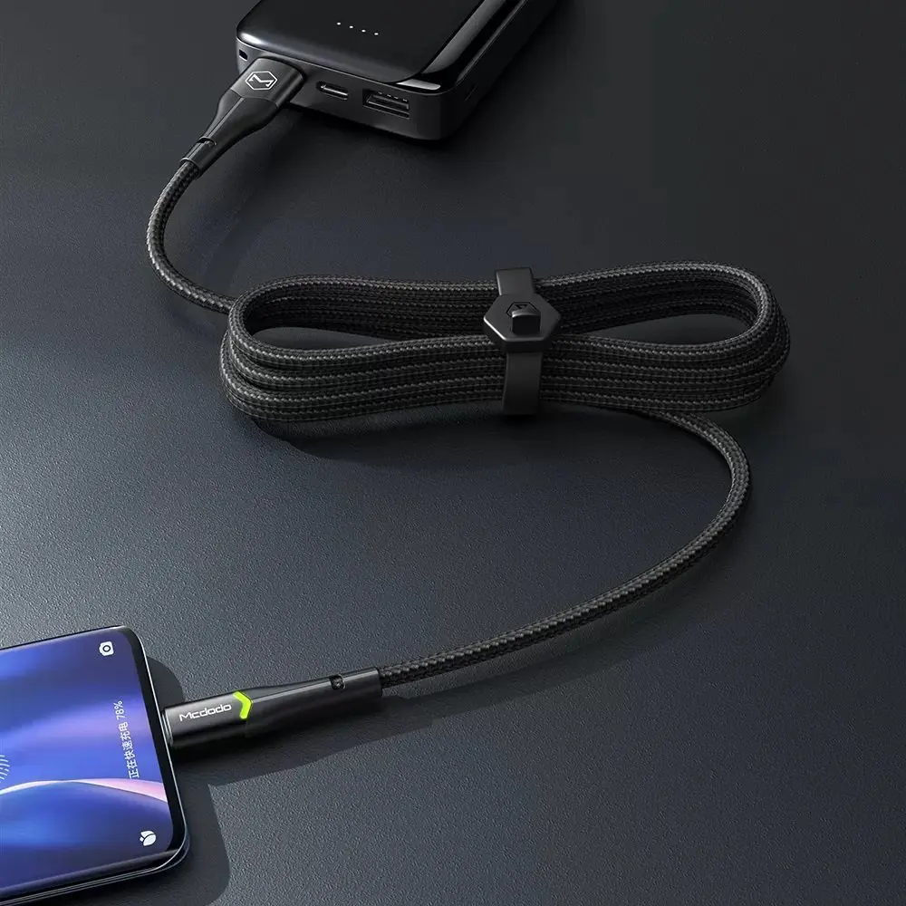 Siyah örgülü bir kablo, telefonu bir powerbank'e bağlıyor. Kablo sarılıdır.