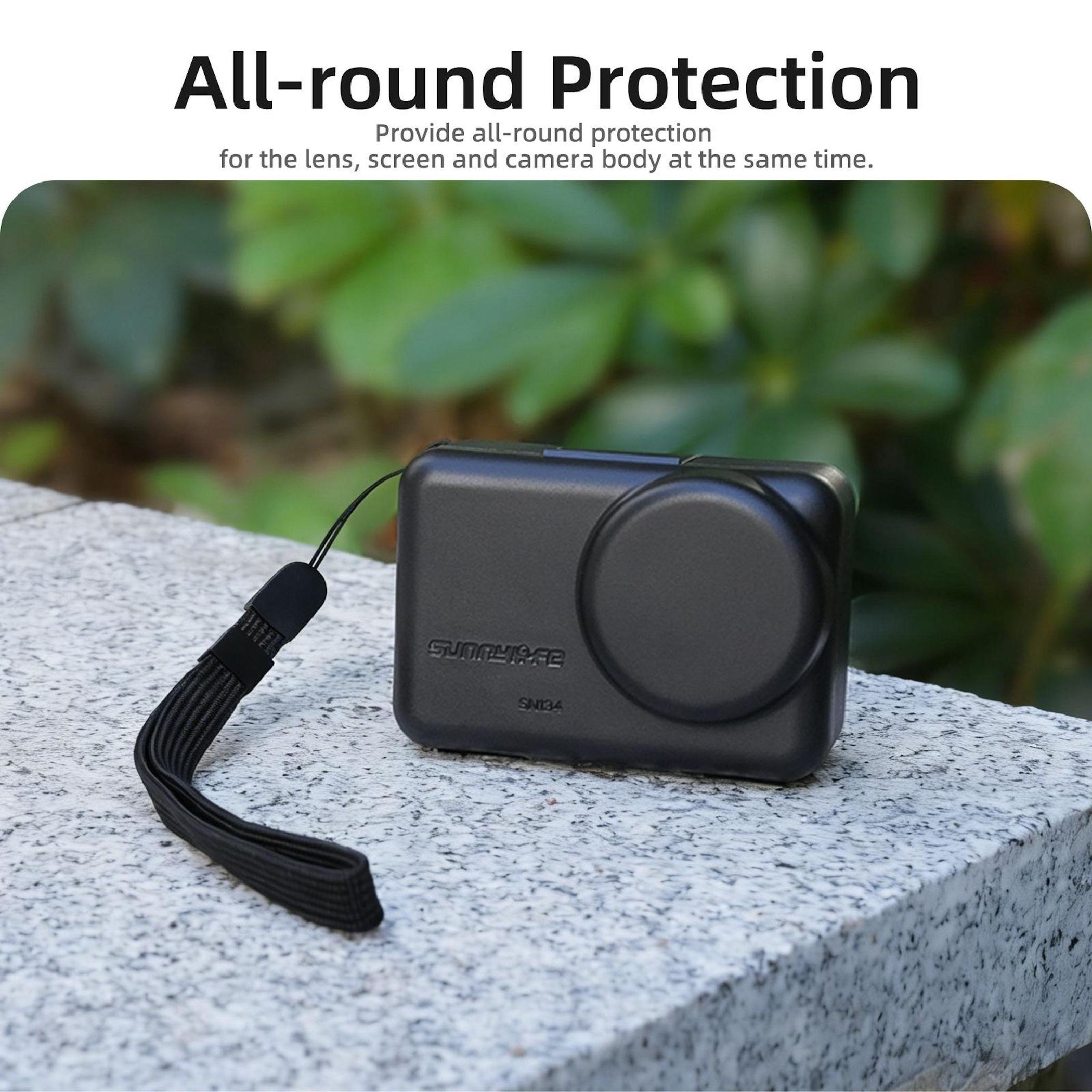 Custodia nera per fotocamera con cinturino su pietra, foglie verdi sullo sfondo.