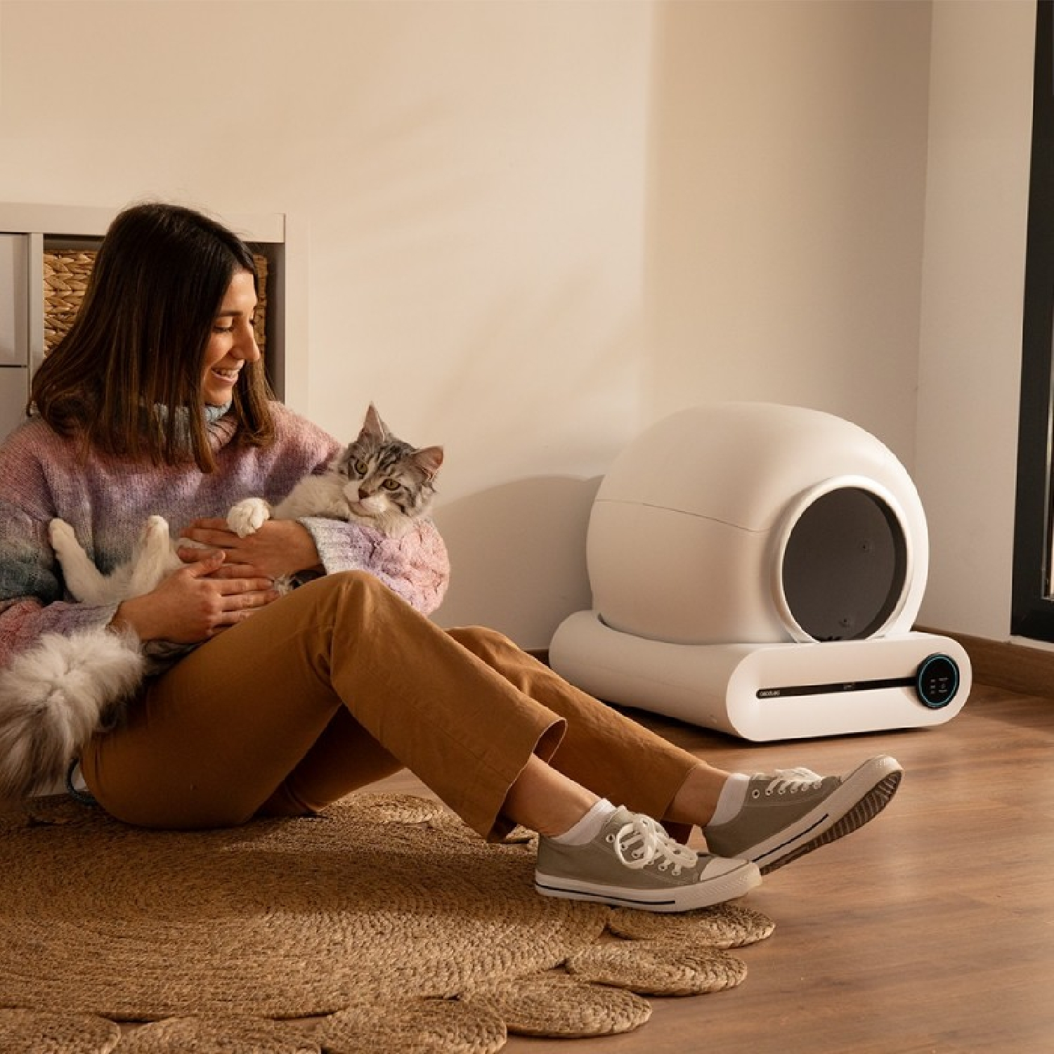 Una mujer sostiene un gato junto a una caja de arena automática.