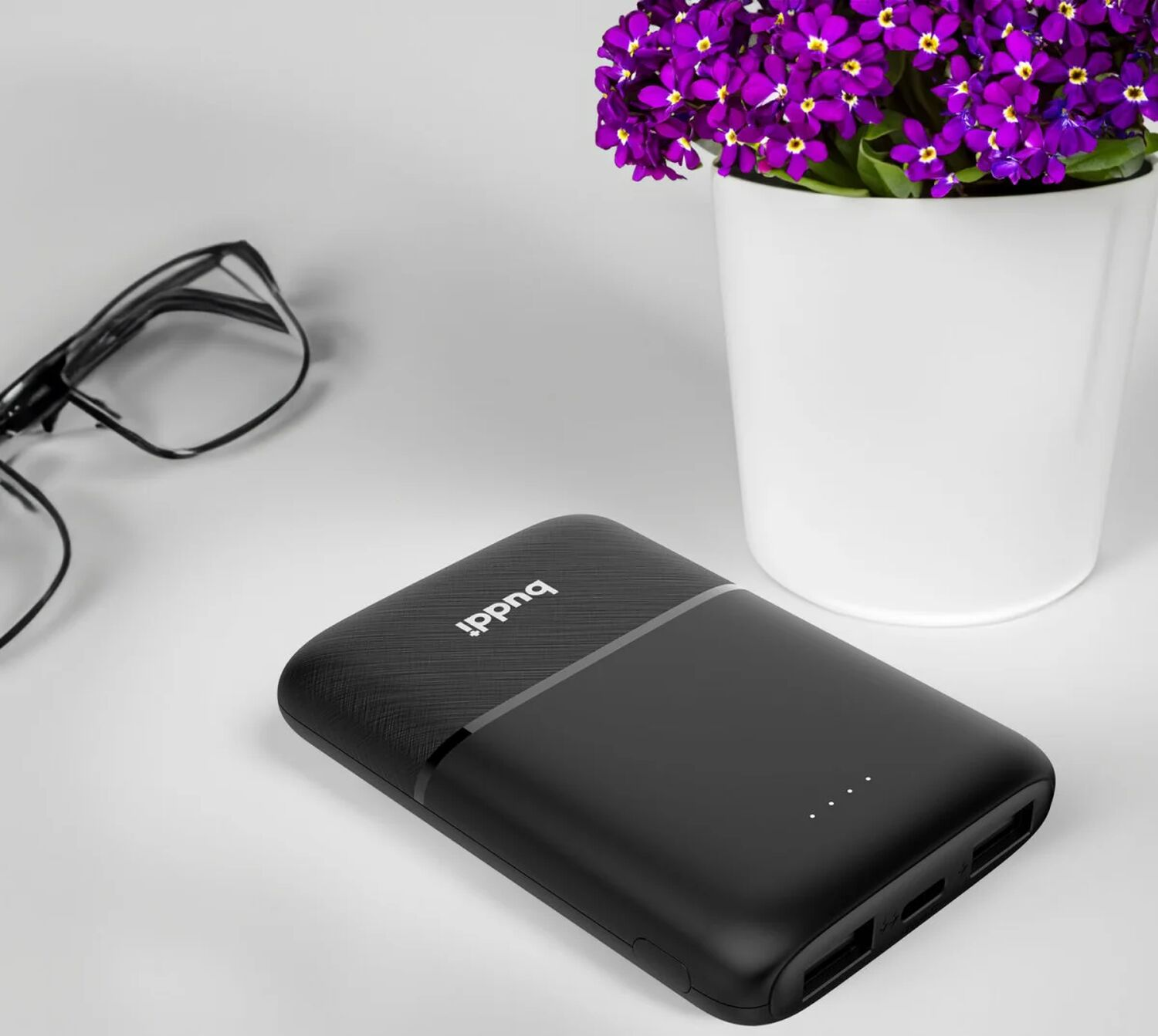 Zwarte powerbank met bril en potplanten op witte tafel.