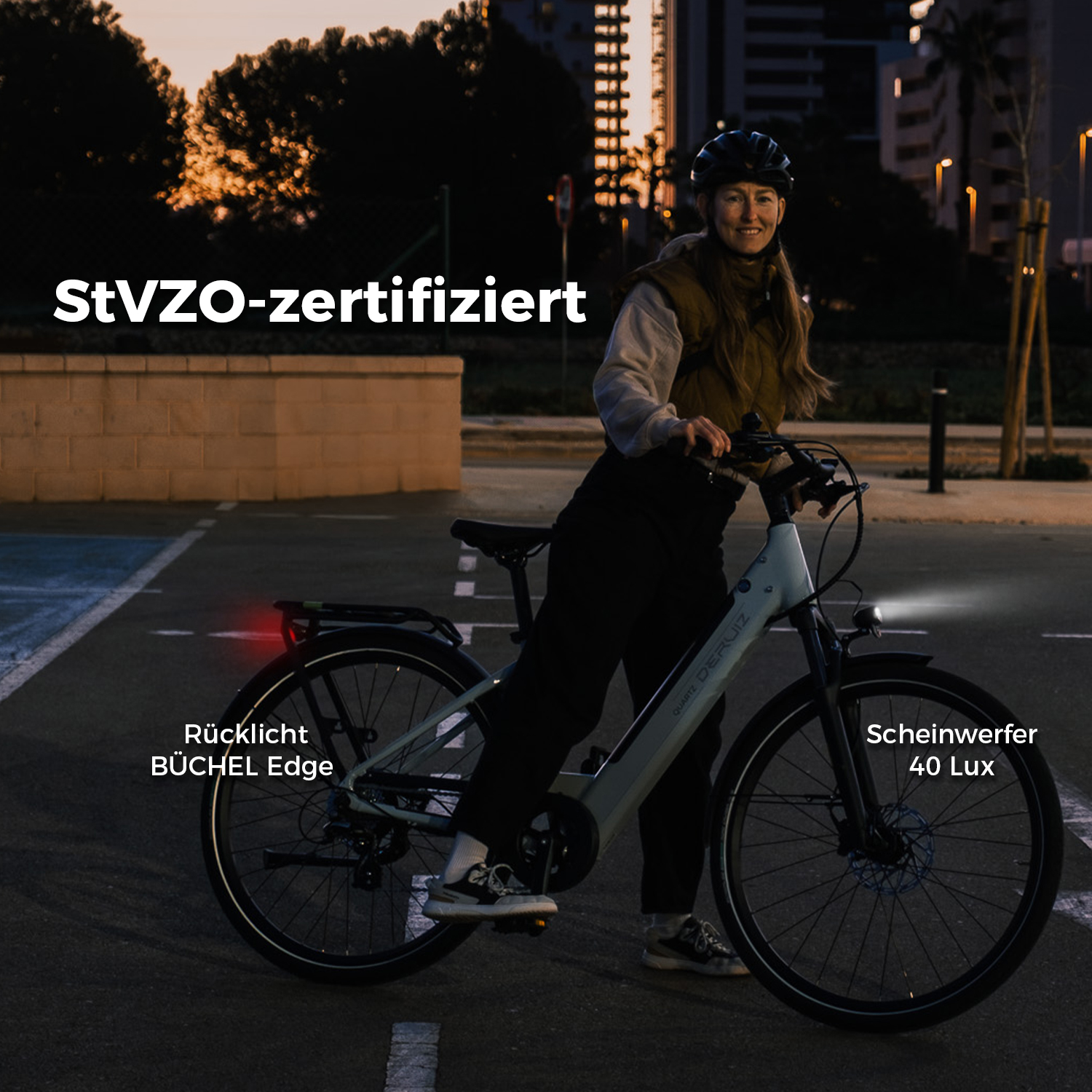 Eine Frau mit Helm fährt ein helles Fahrrad mit Beleuchtung bei Sonnenuntergang.
