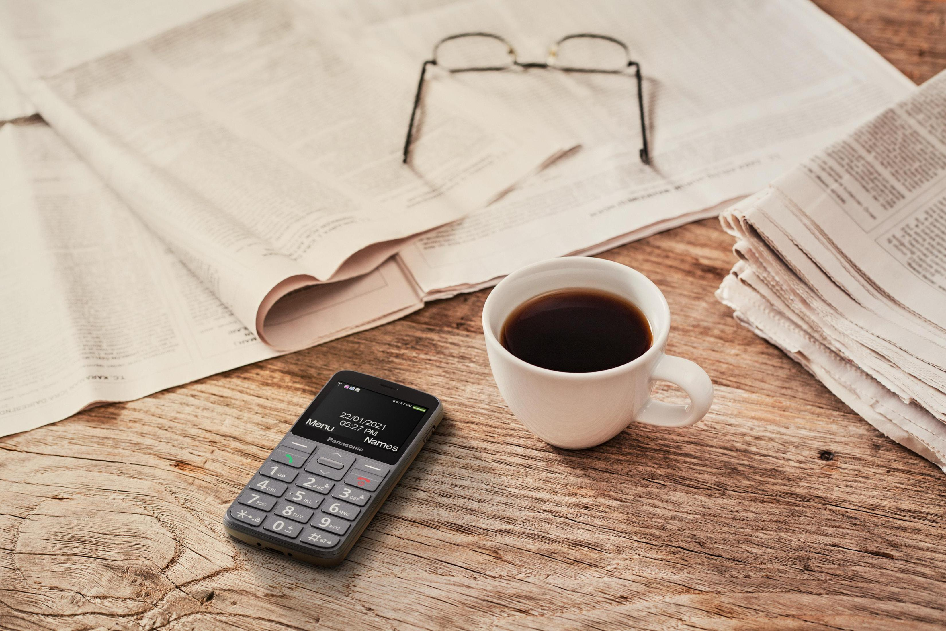 Ein Handy, eine Kaffeetasse und Zeitungen auf einem Holztisch.