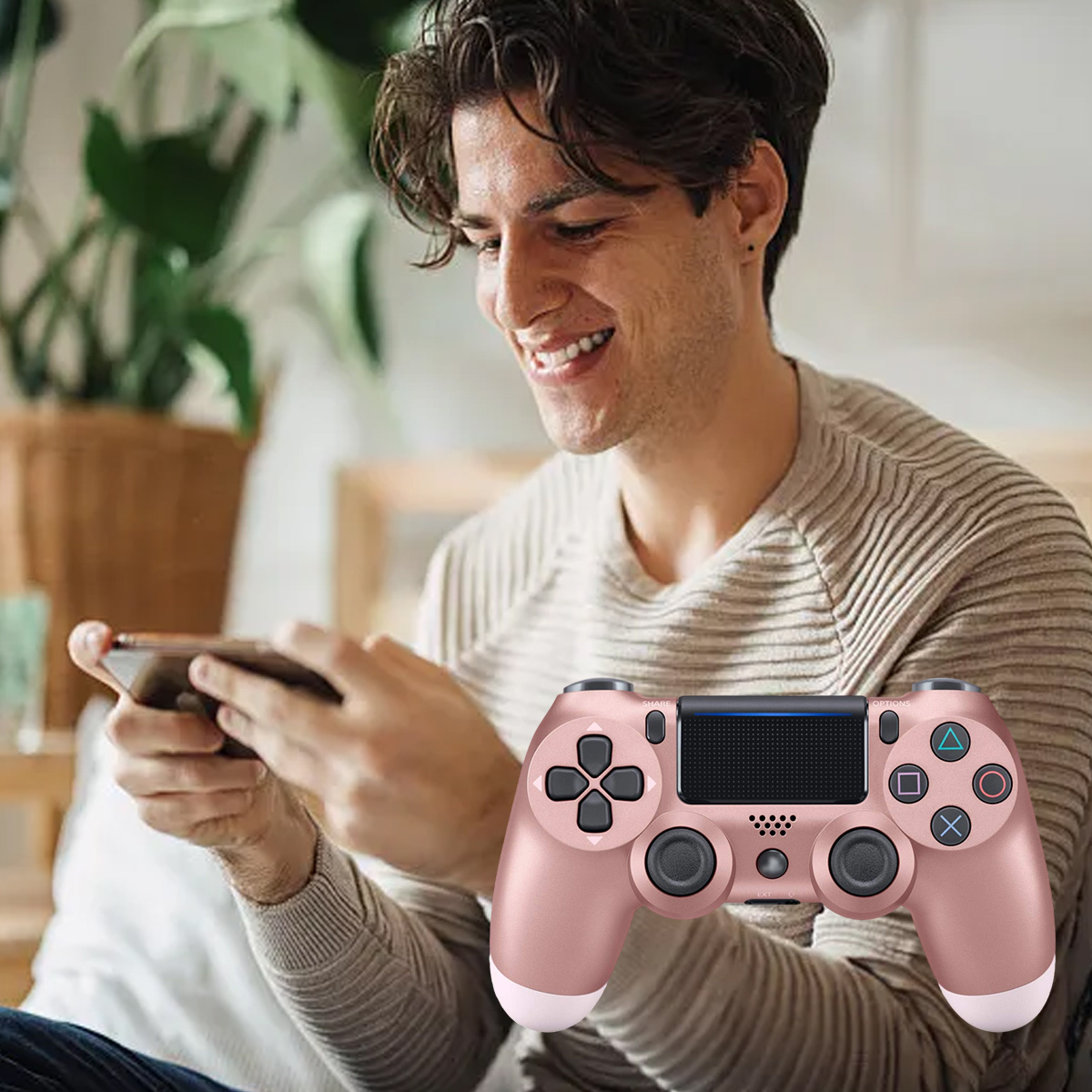 Ein Mann spielt mit einem Controller und einem Handy. Er lächelt.