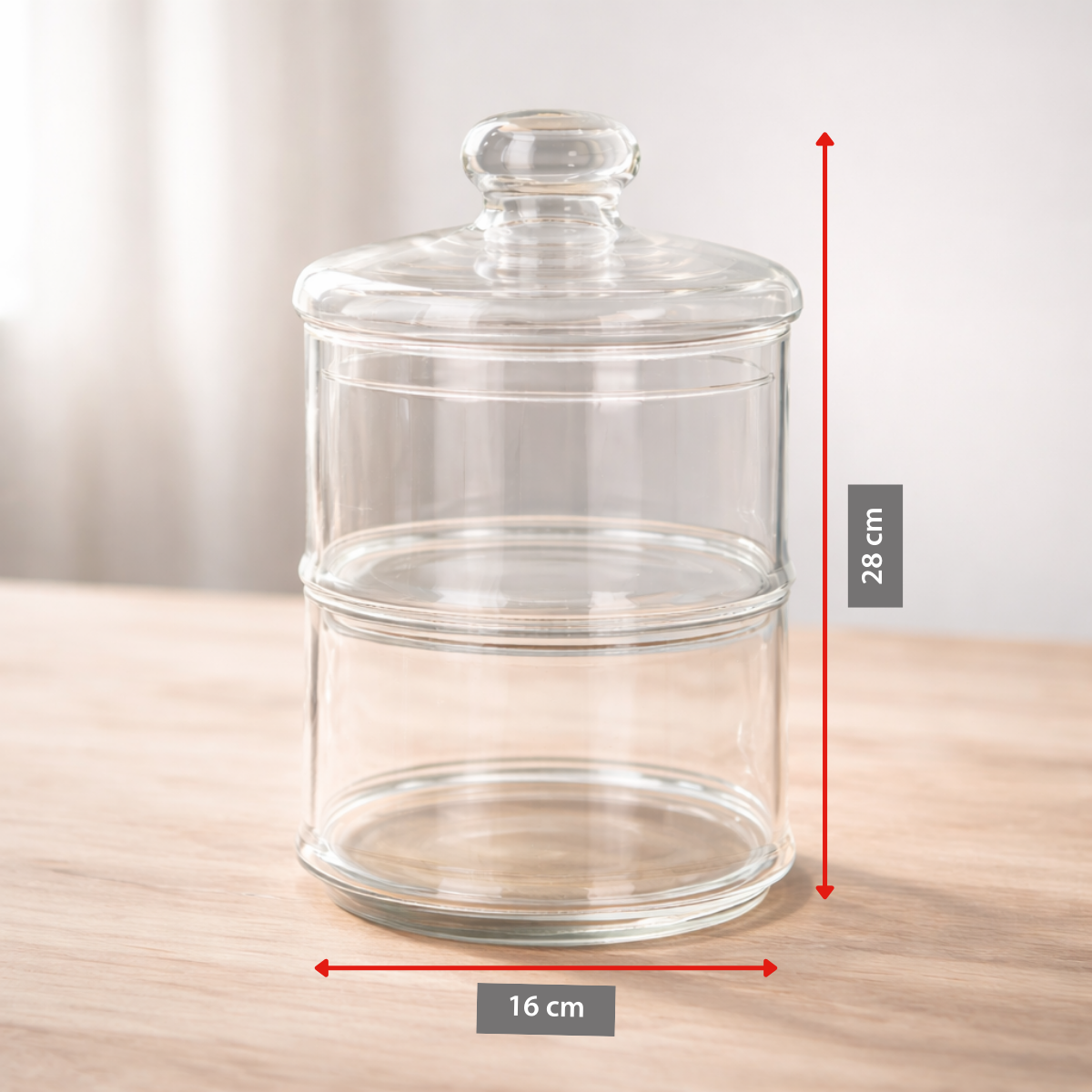 A clear, two-tiered glass container with a lid sits on a wooden table.