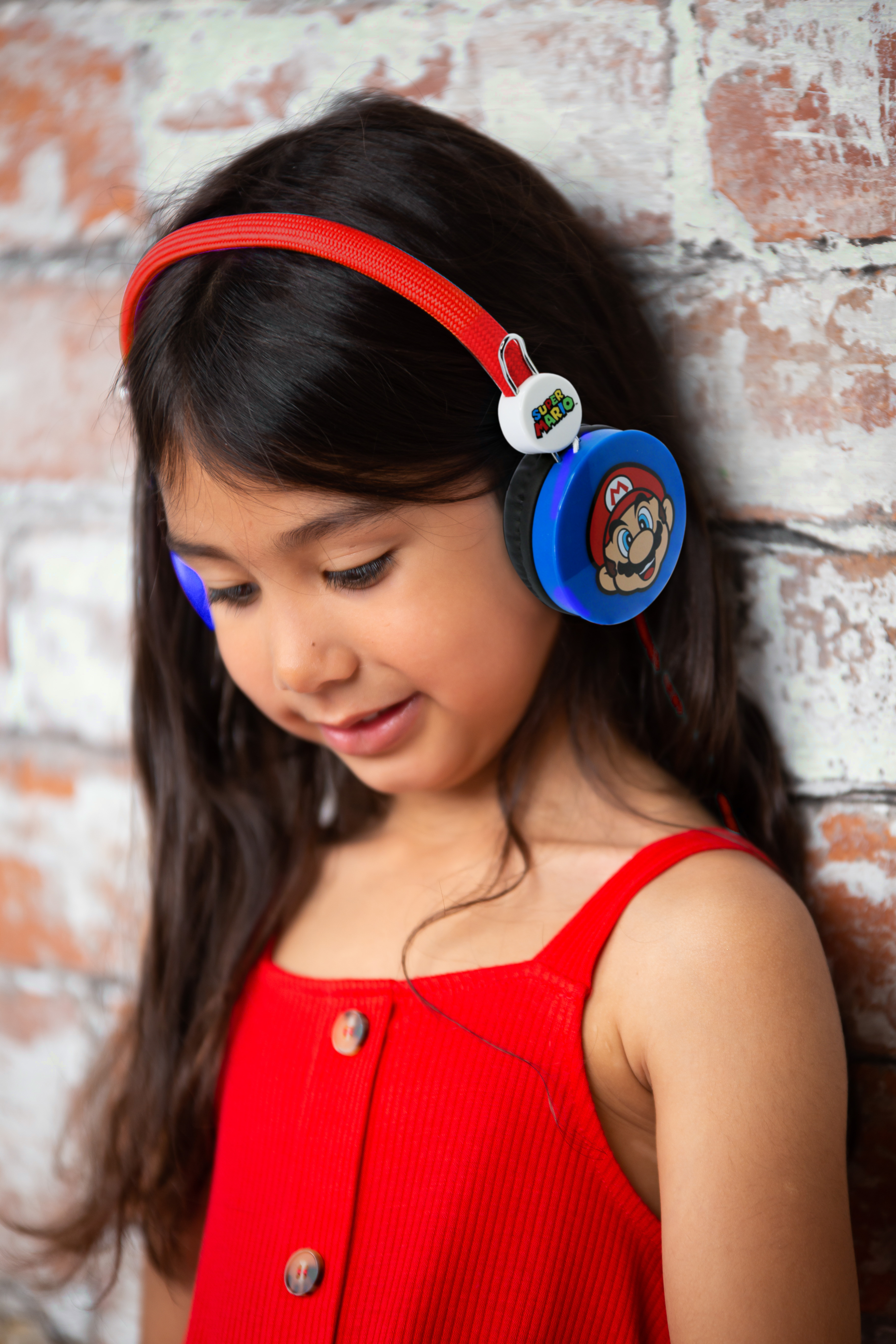 Una bambina con cuffie Super Mario appoggiata a un muro di mattoni.