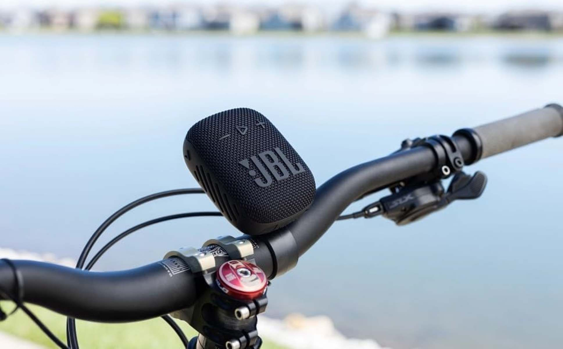 Un altoparlante JBL nero è fissato al manubrio di una bicicletta. Sullo sfondo c'è acqua.