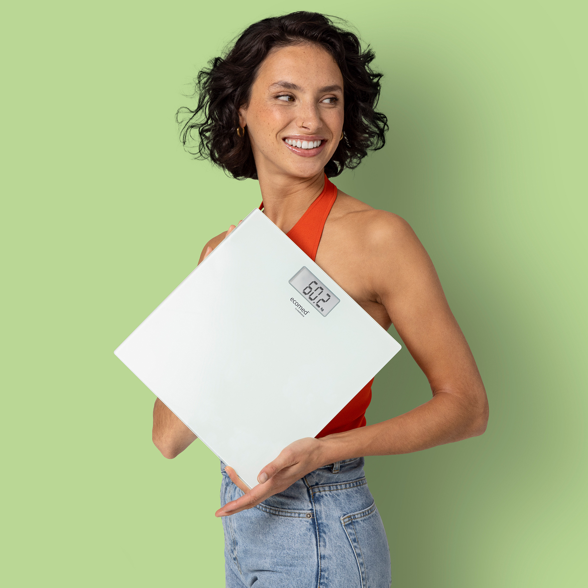 Eine Frau mit kurzen dunklen Haaren hält eine weiße Waage mit der Anzeige 60,2 kg.