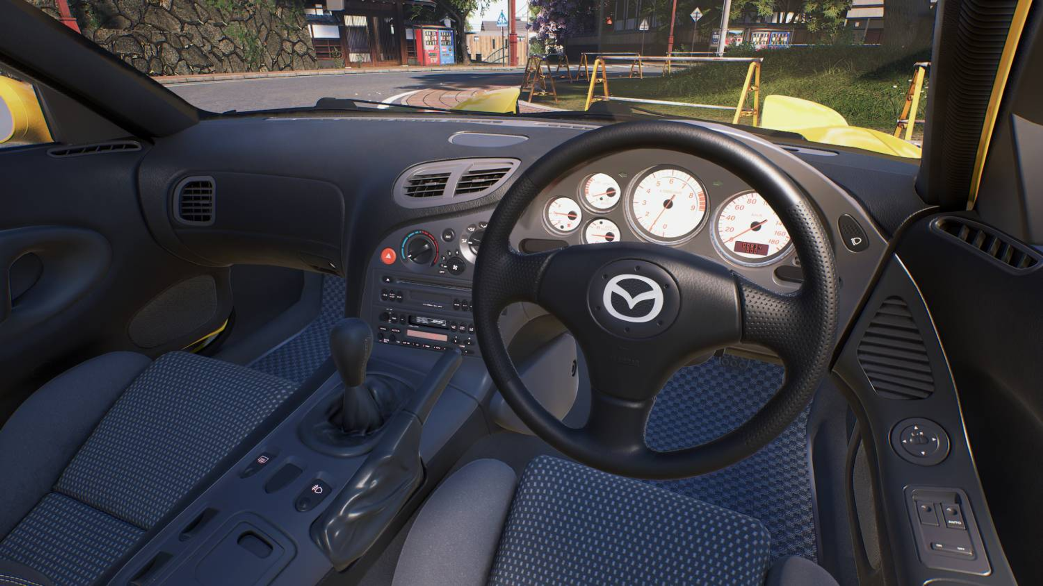 Vista interna di una Mazda RX-7 gialla, con volante e cruscotto.