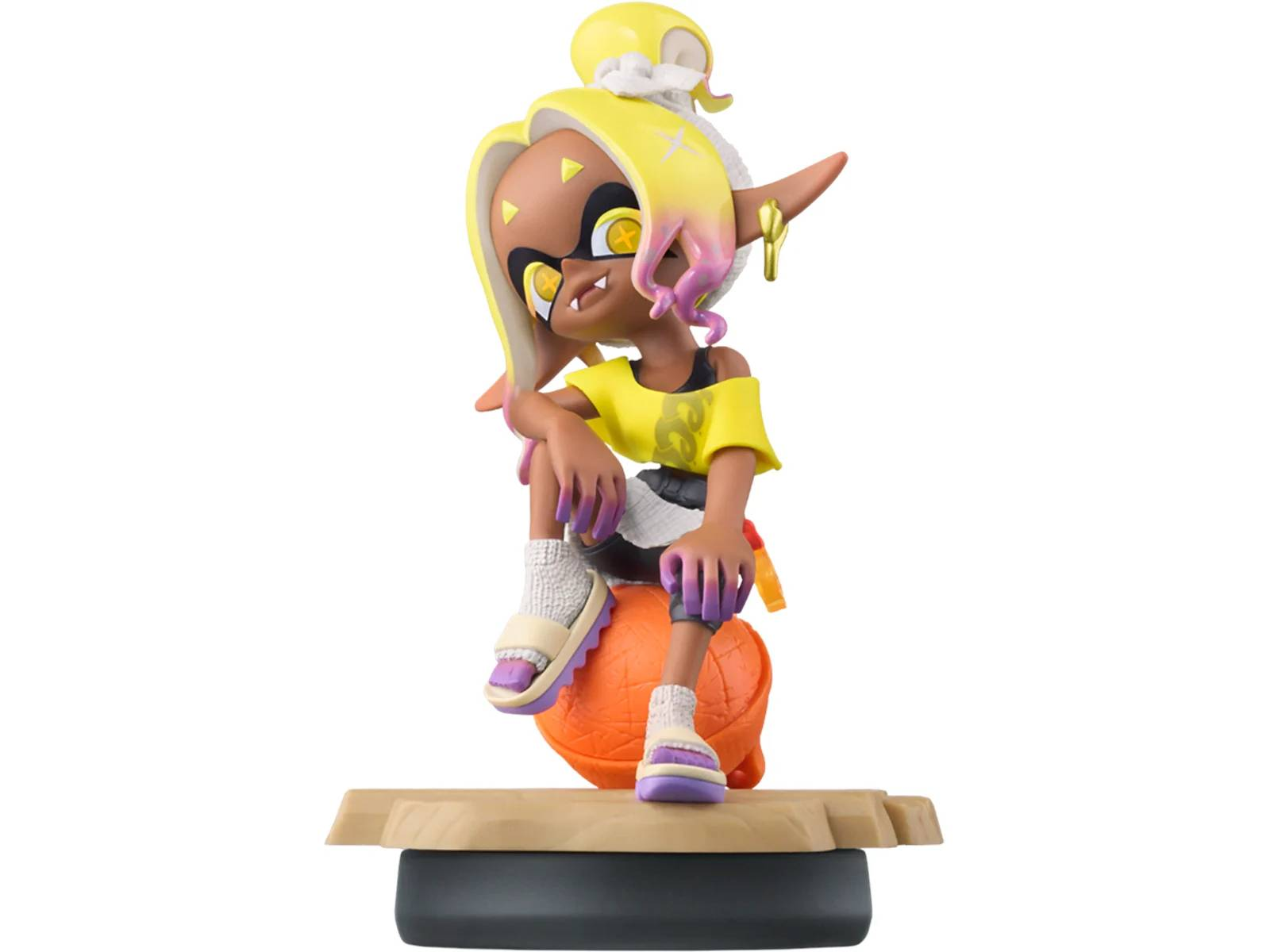 Una figura con pelo amarillo se sienta en una pelota naranja, viste un top amarillo.