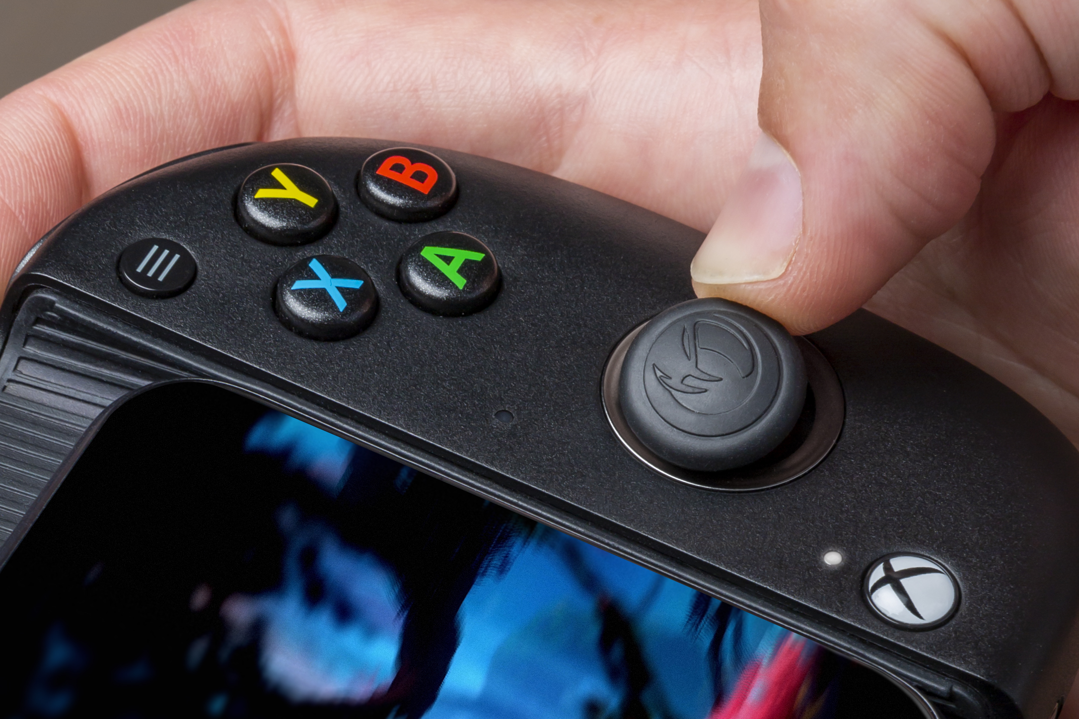 Nahaufnahme eines Controllers mit Daumen auf dem rechten Stick. Grüne, rote, gelbe und blaue Tasten.