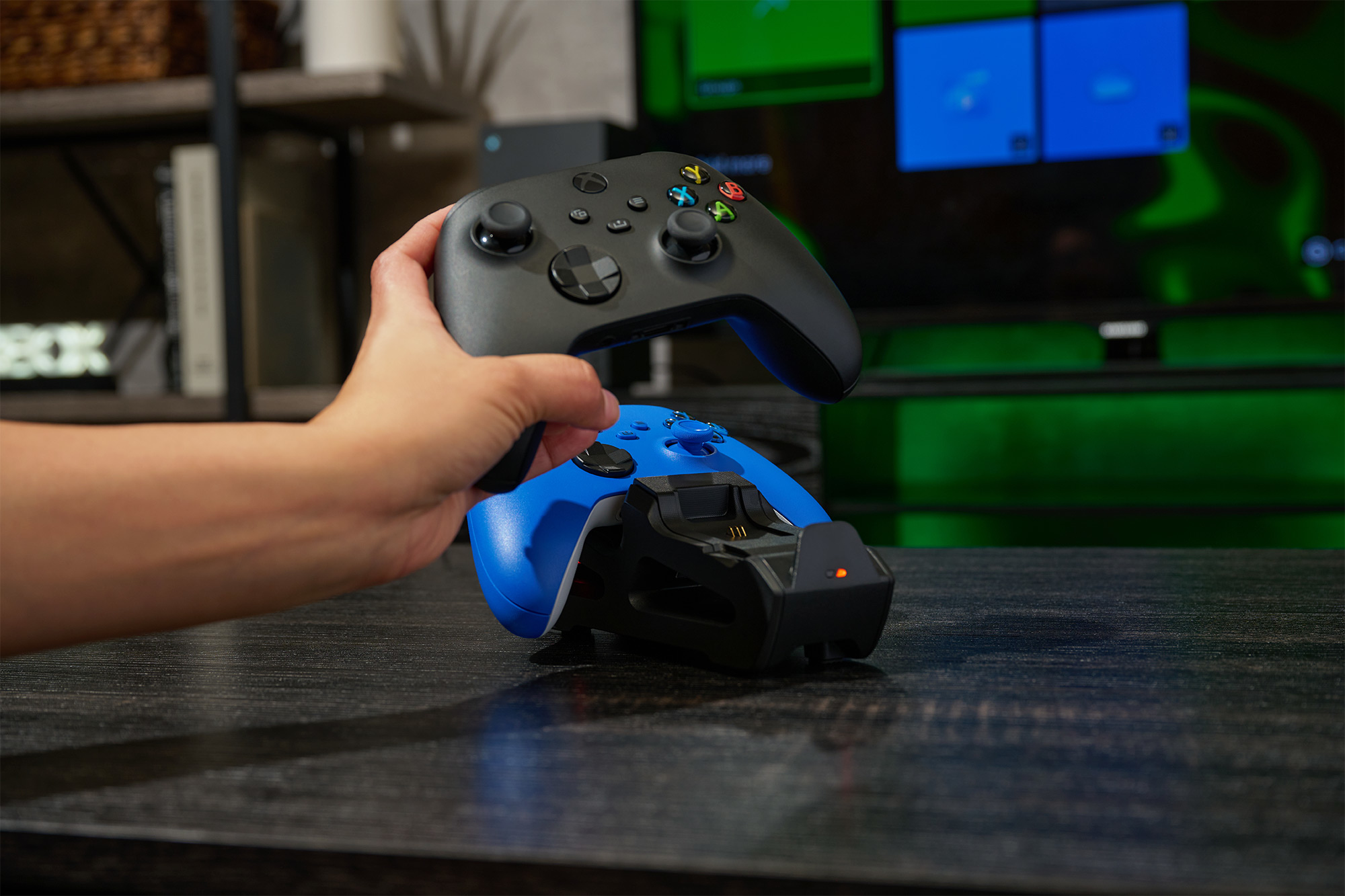 Eine Hand hält einen schwarzen Controller über eine blaue Controller-Ladestation.