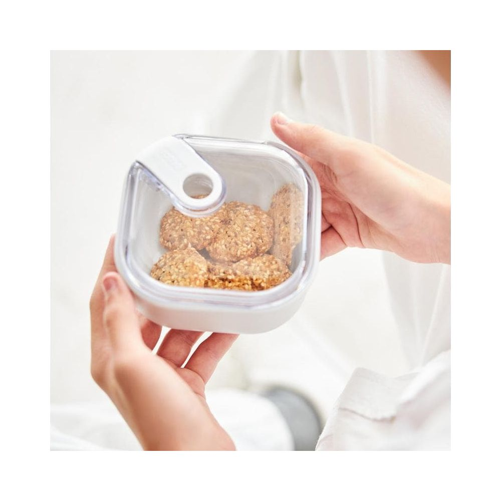 Mani tengono un contenitore trasparente pieno di biscotti rotondi.