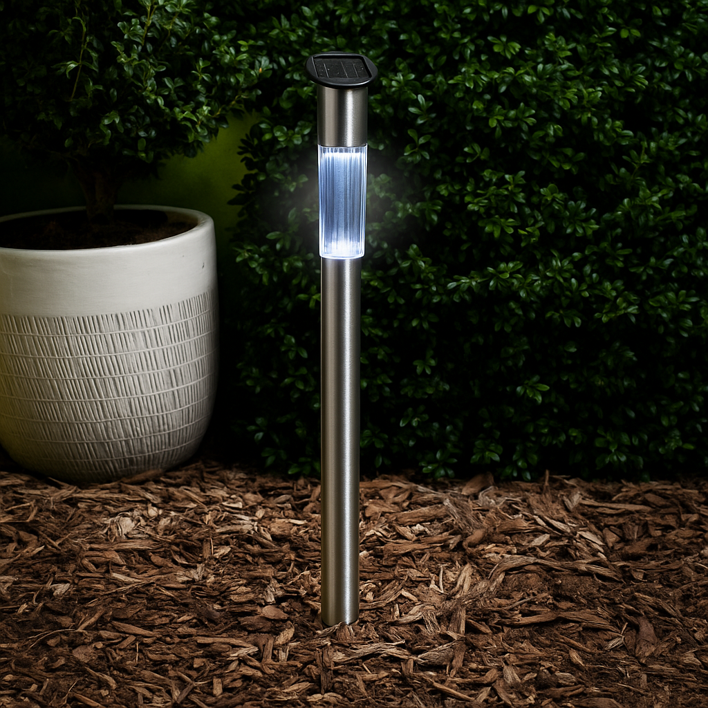 Een metalen solar tuinlamp met witte gloed staat naast een pot en struiken.