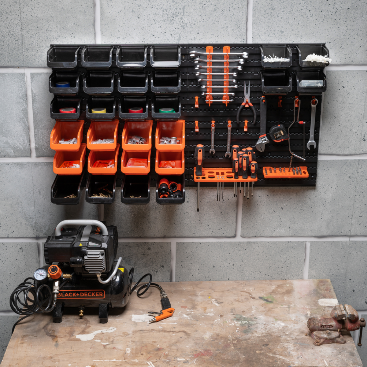 Gereedschapswand met bakken, gereedschap, compressor en werkbank.