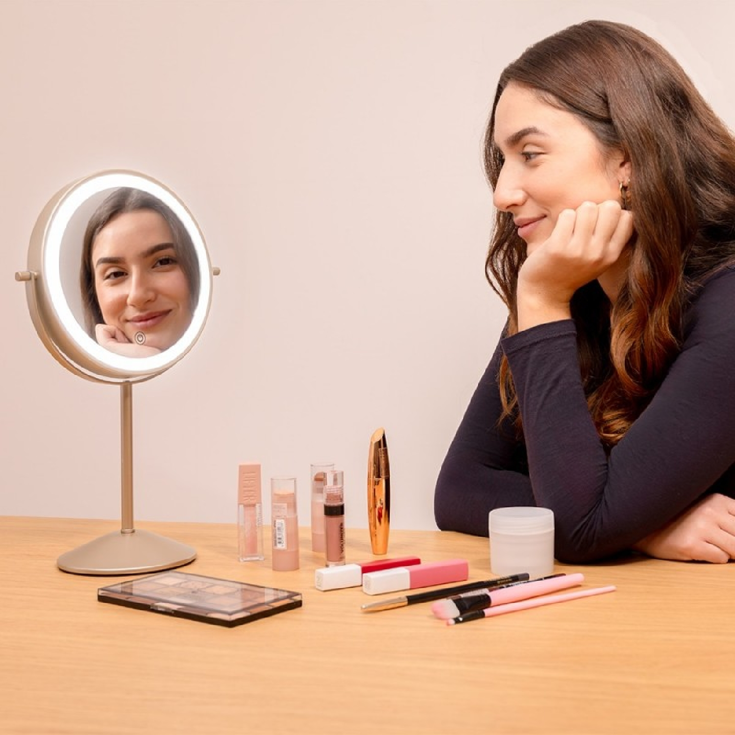 Una mujer mira un espejo de maquillaje iluminado rodeado de cosméticos.