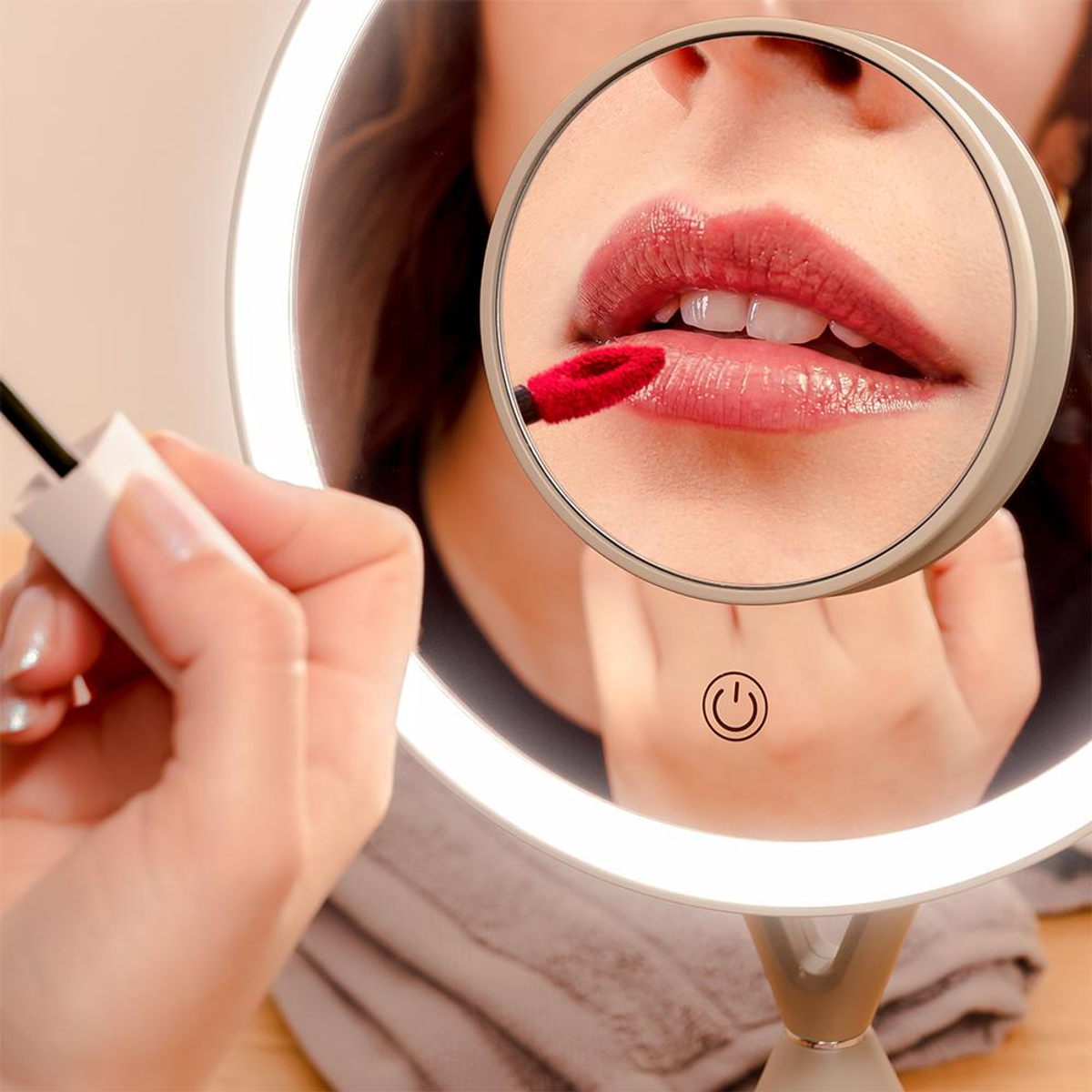 Una mano con lápiz labial rojo se aplica maquillaje, reflejada en un espejo iluminado.